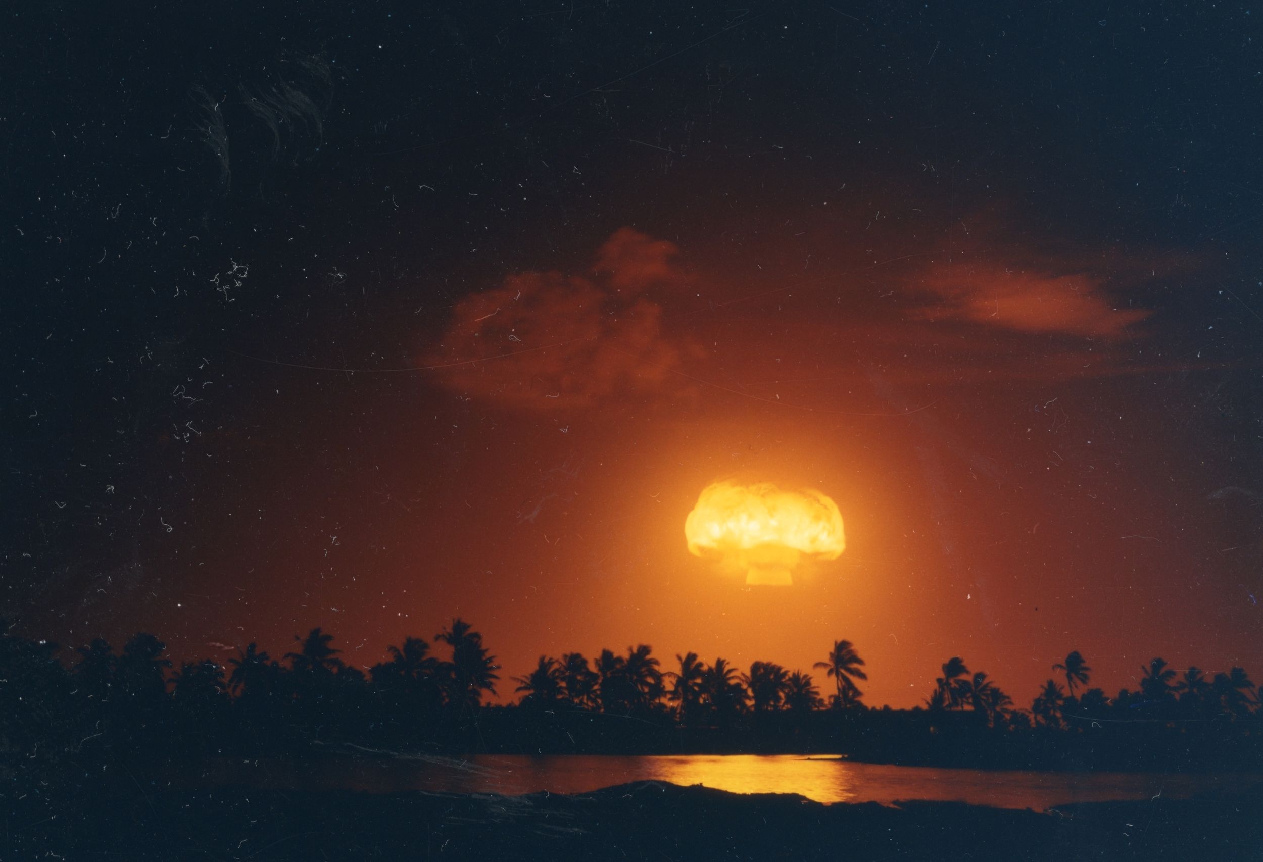 Bluegill detonation fireball over Christmas Island with palm trees and the lagoon in the foreground.