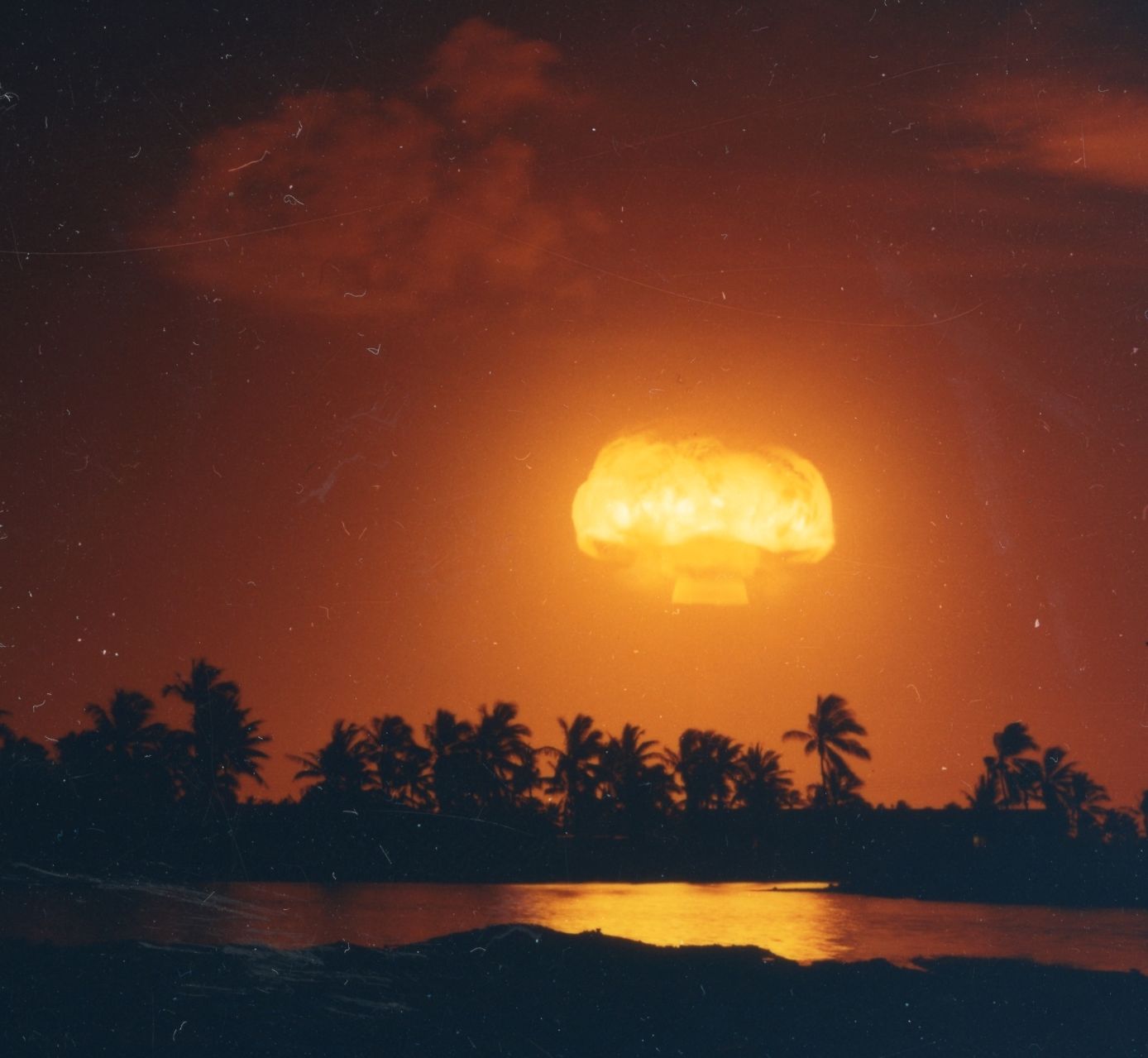 Bluegill detonation fireball over Christmas Island with palm trees and the lagoon in the foreground.