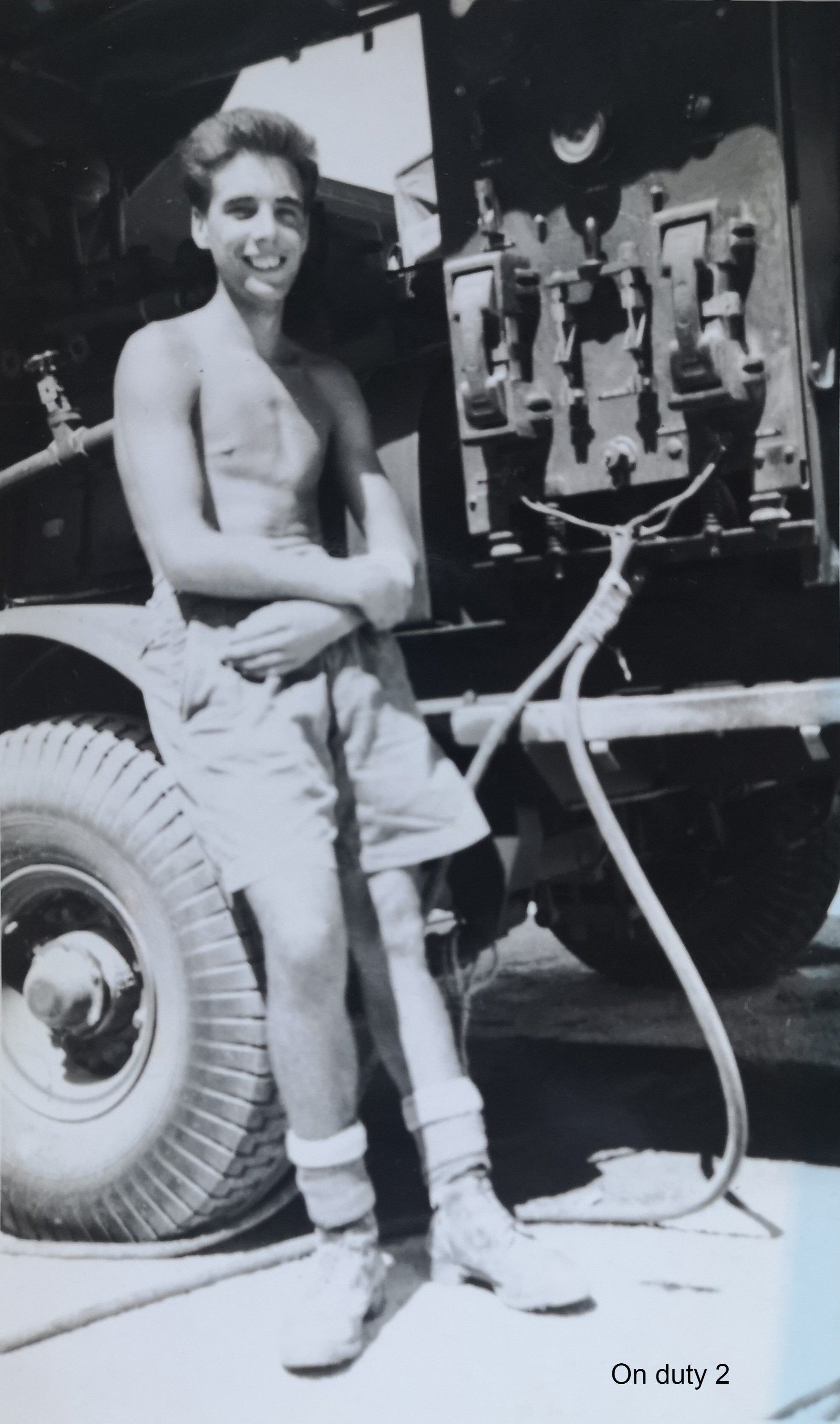 John Morris in shorts and boots, standing next to a large refuelling truck.