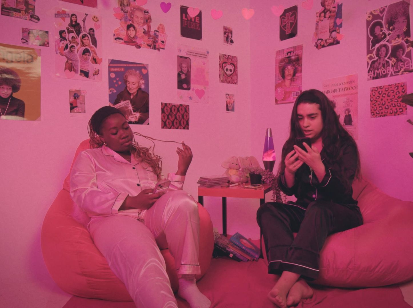 Two young women looking at their phones in a pink room.