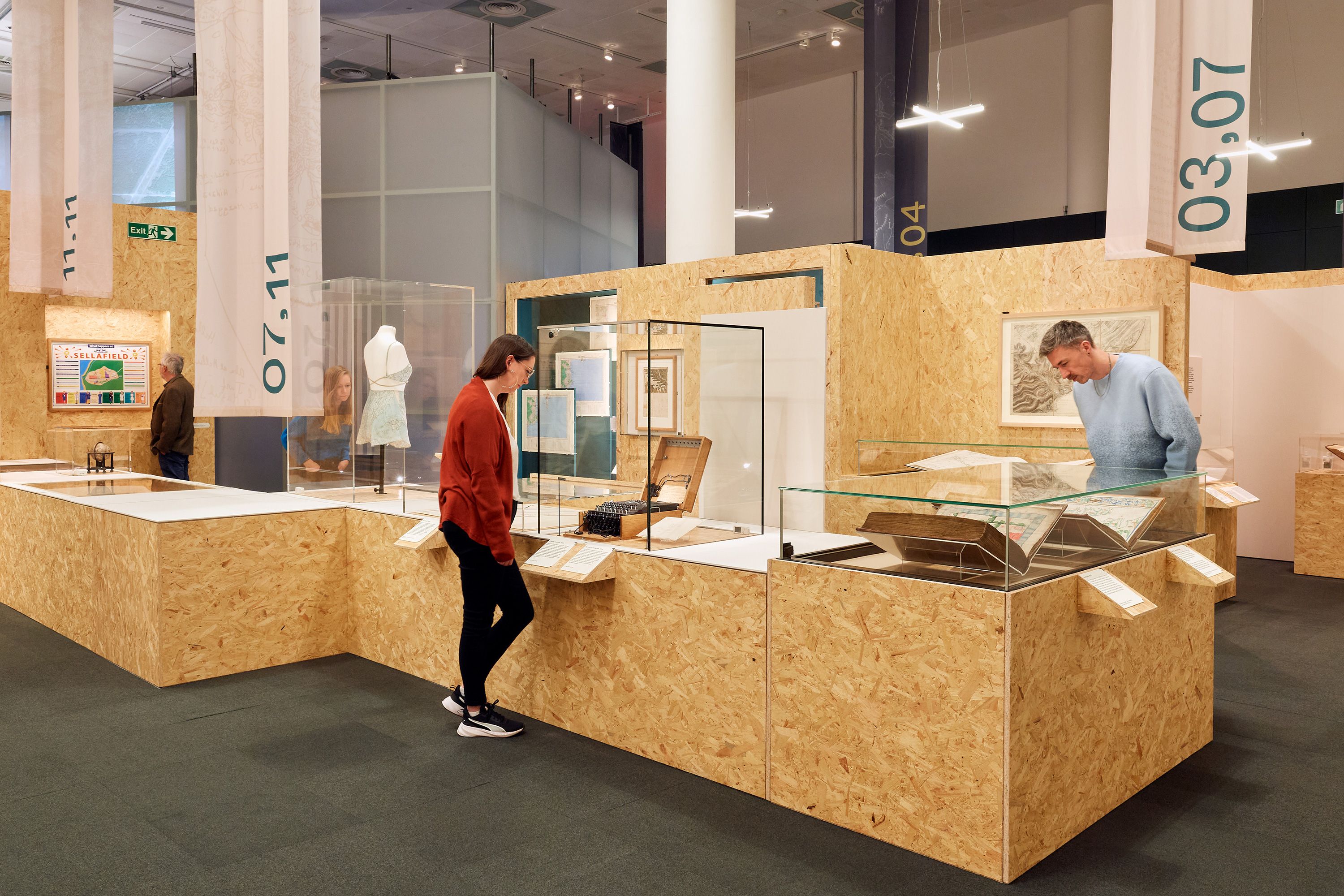 Visitors to the Secret Maps exhibition at the British Library, looking through glass cases in an exhibition space at a number of ornate maps.
