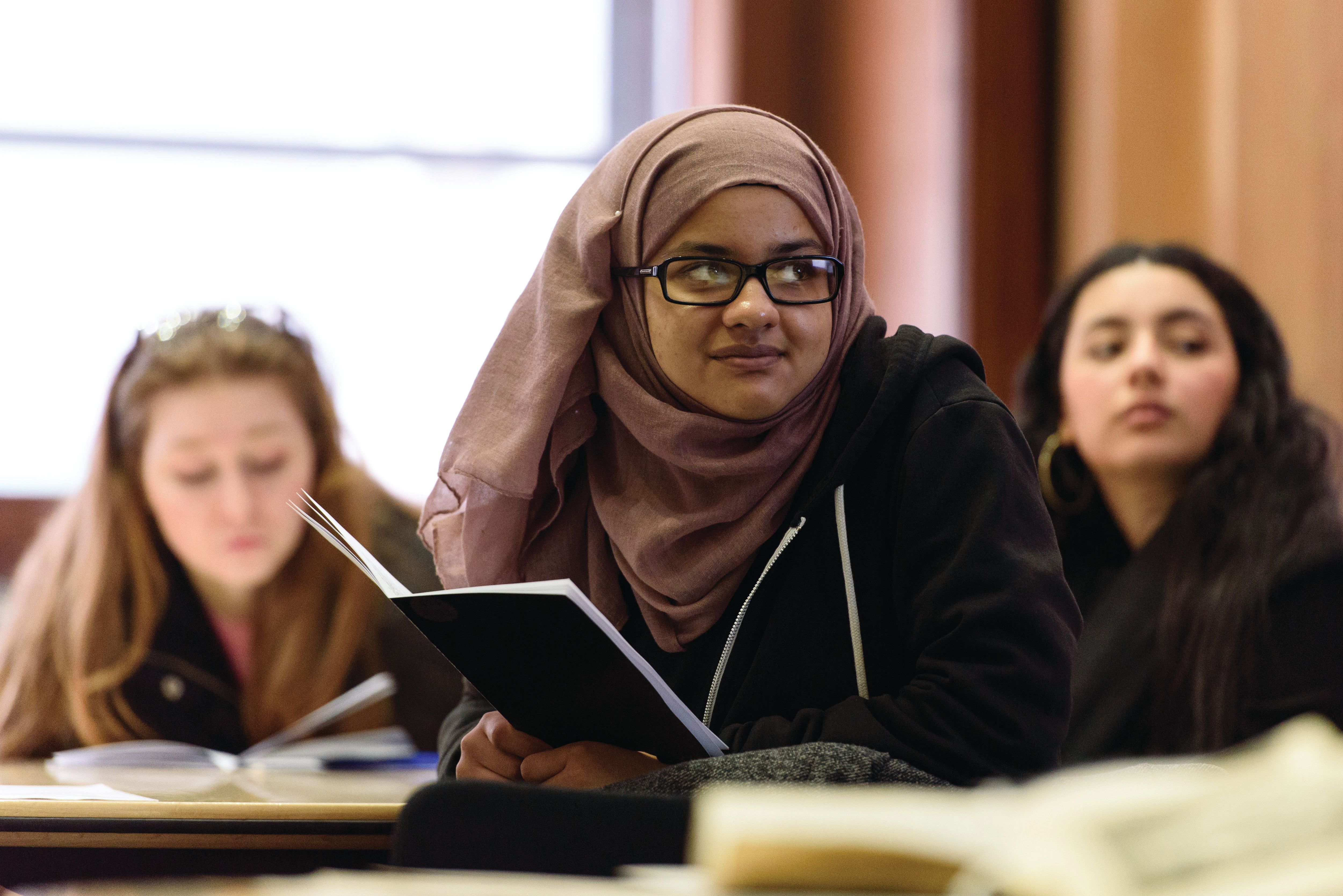 Three young people sat at desks in a secondary school classroom.