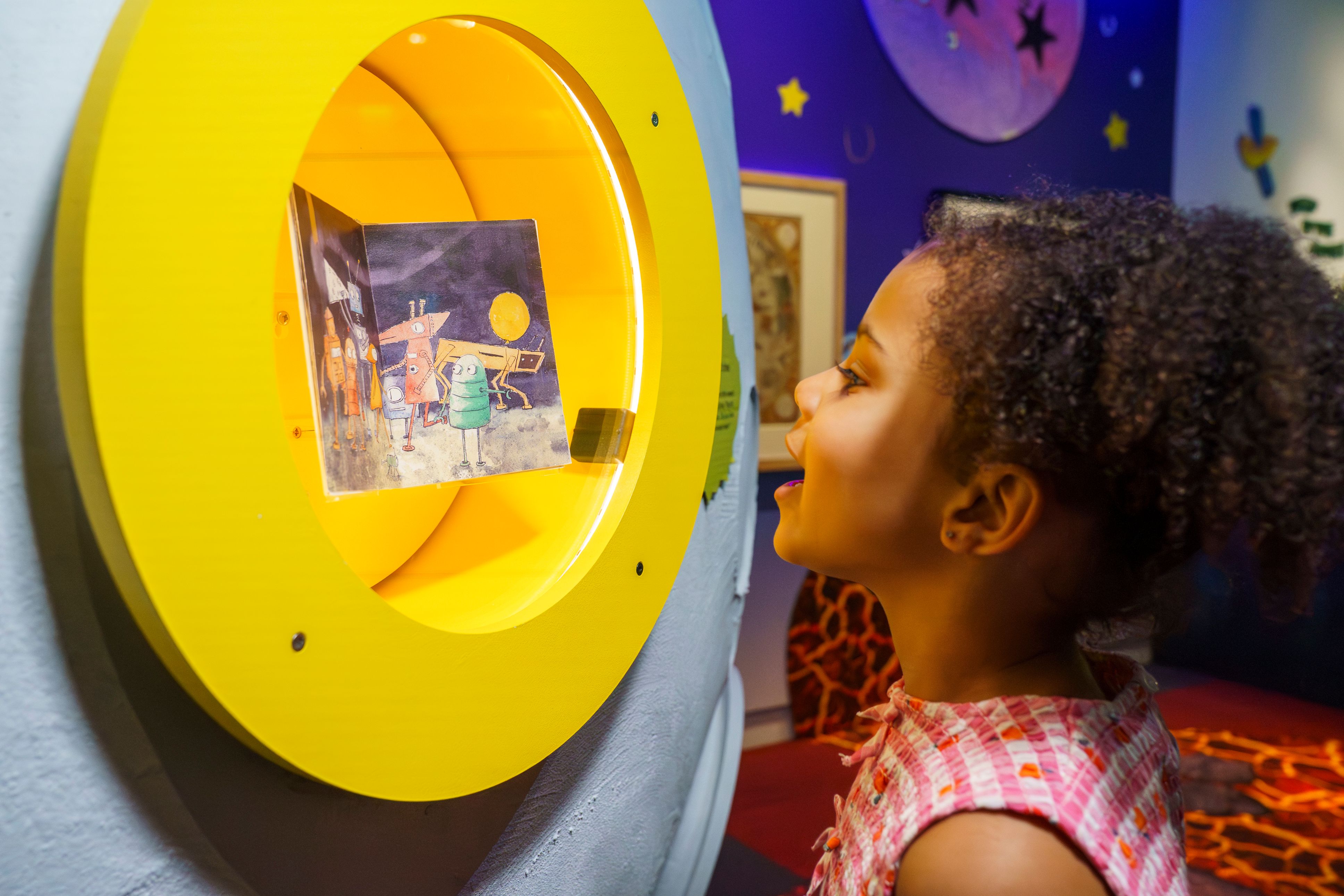 A girl looking at a book in a round yellow display case.