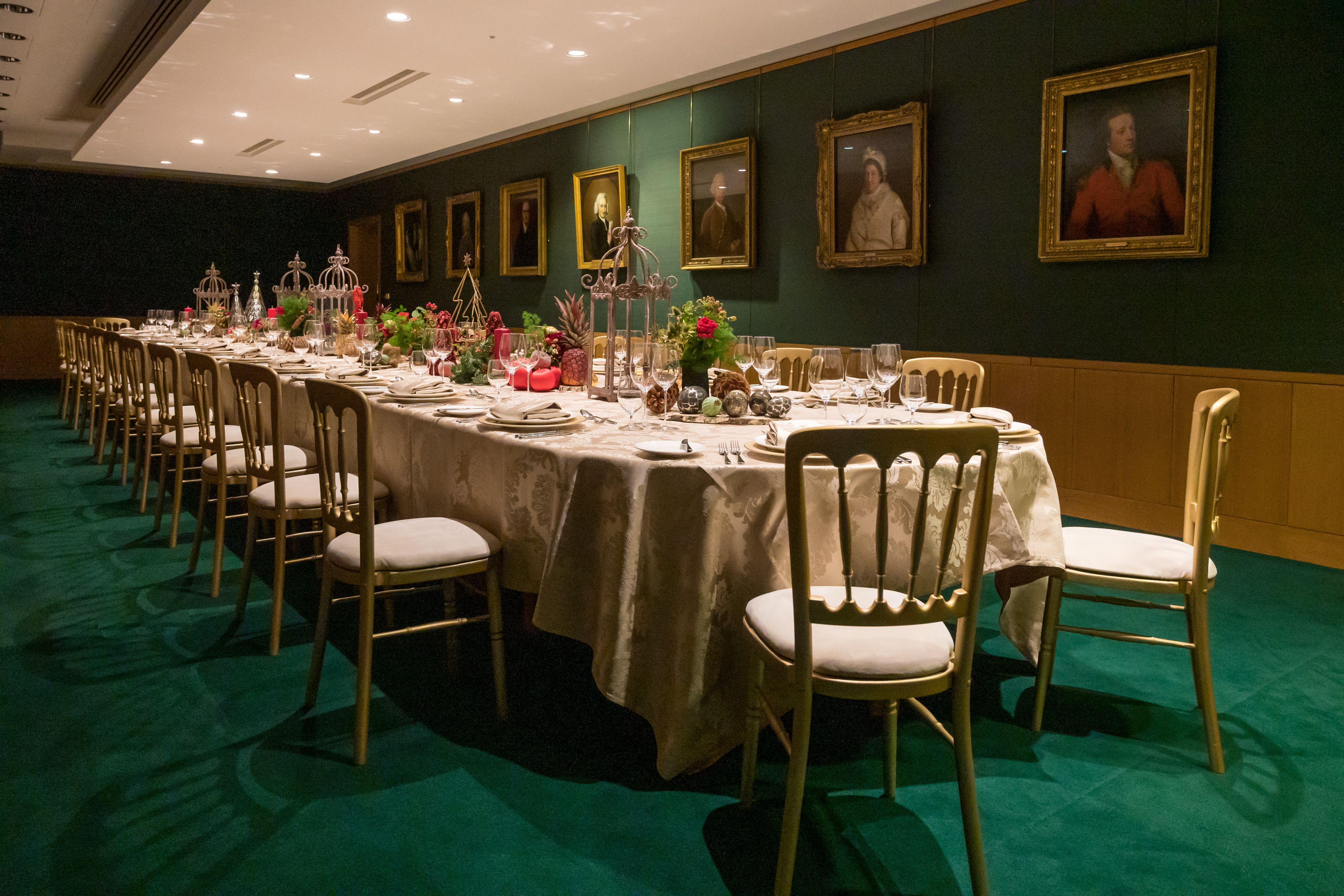 A large table set up in the Boardroom surrounded by portraits on the wall.