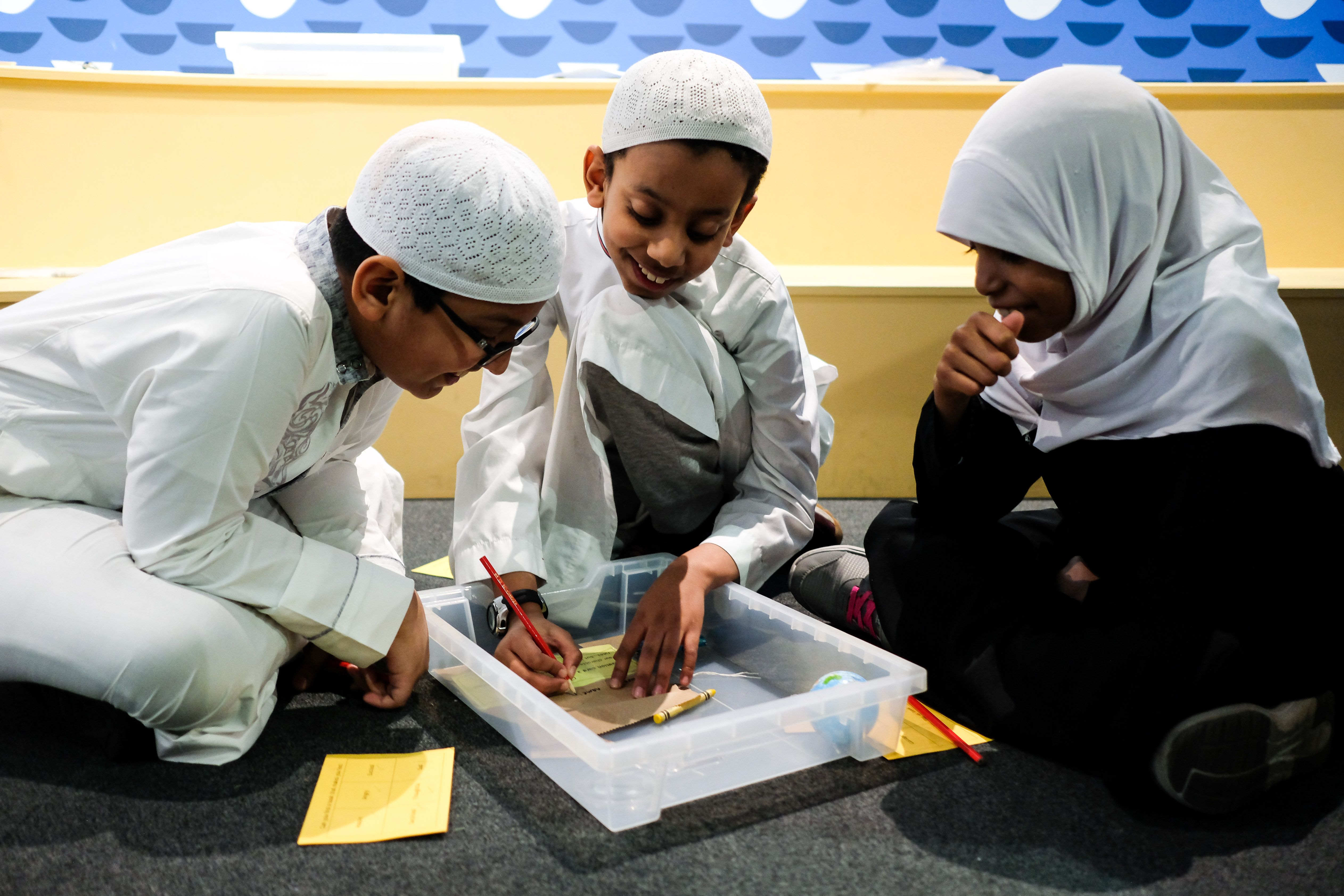 Three school children sit on the floor, taking part in a British Library schools activity.