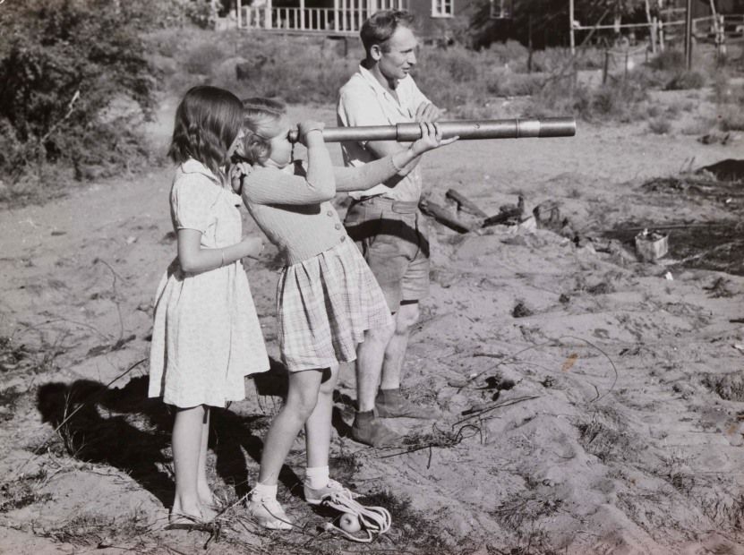 Two girls watch the detonation of the first British atomic bomb through a telescope whilst on the beach.