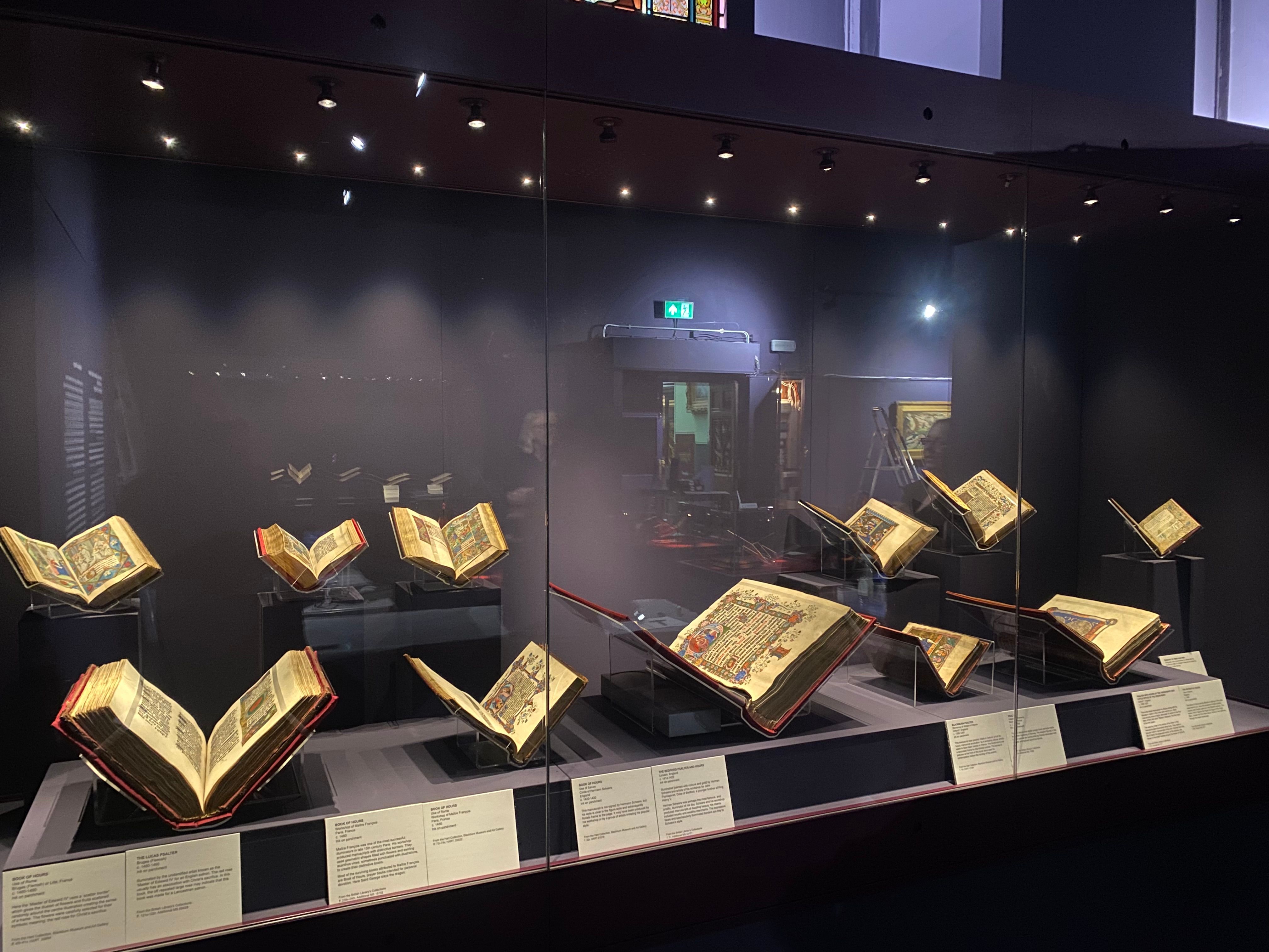 A glass case, enclosing 11 open medieval manuscripts placed on Perspex bookstands.