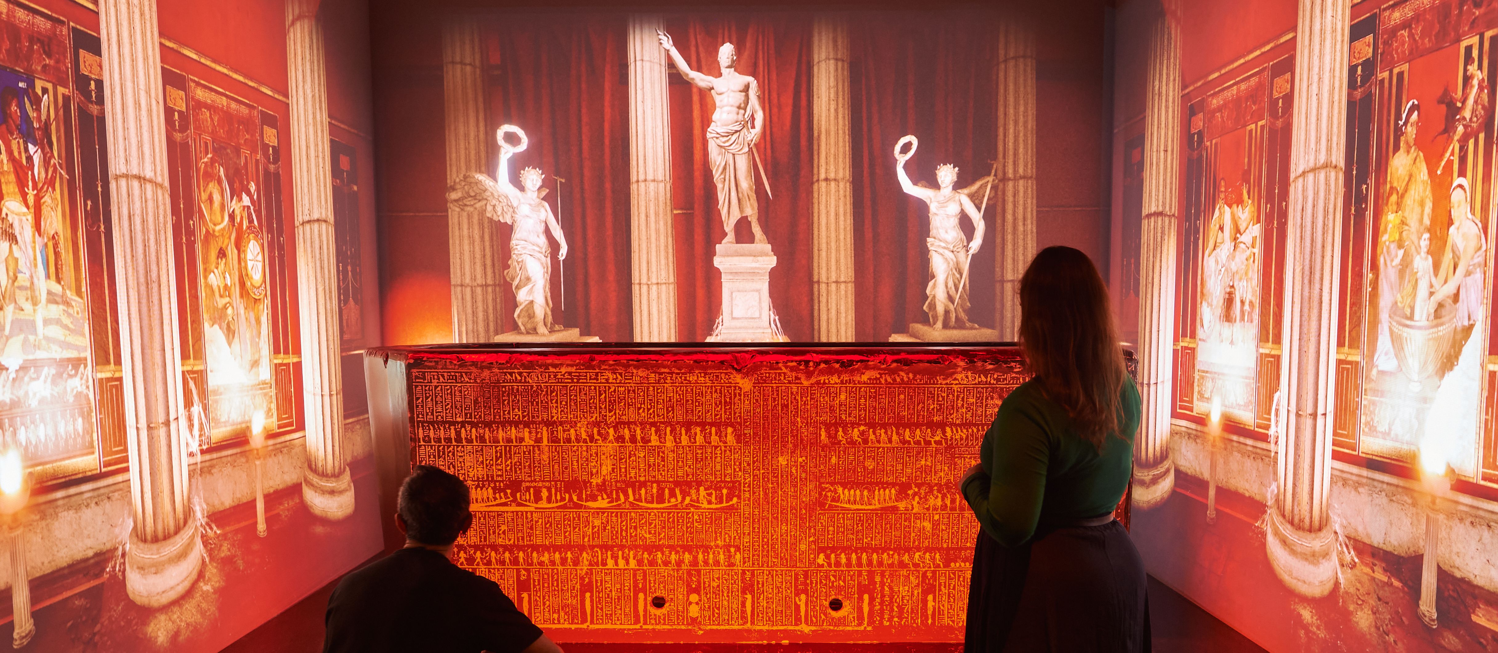 Two visitors stand in front of an illuminated display at a British Library exhibition.