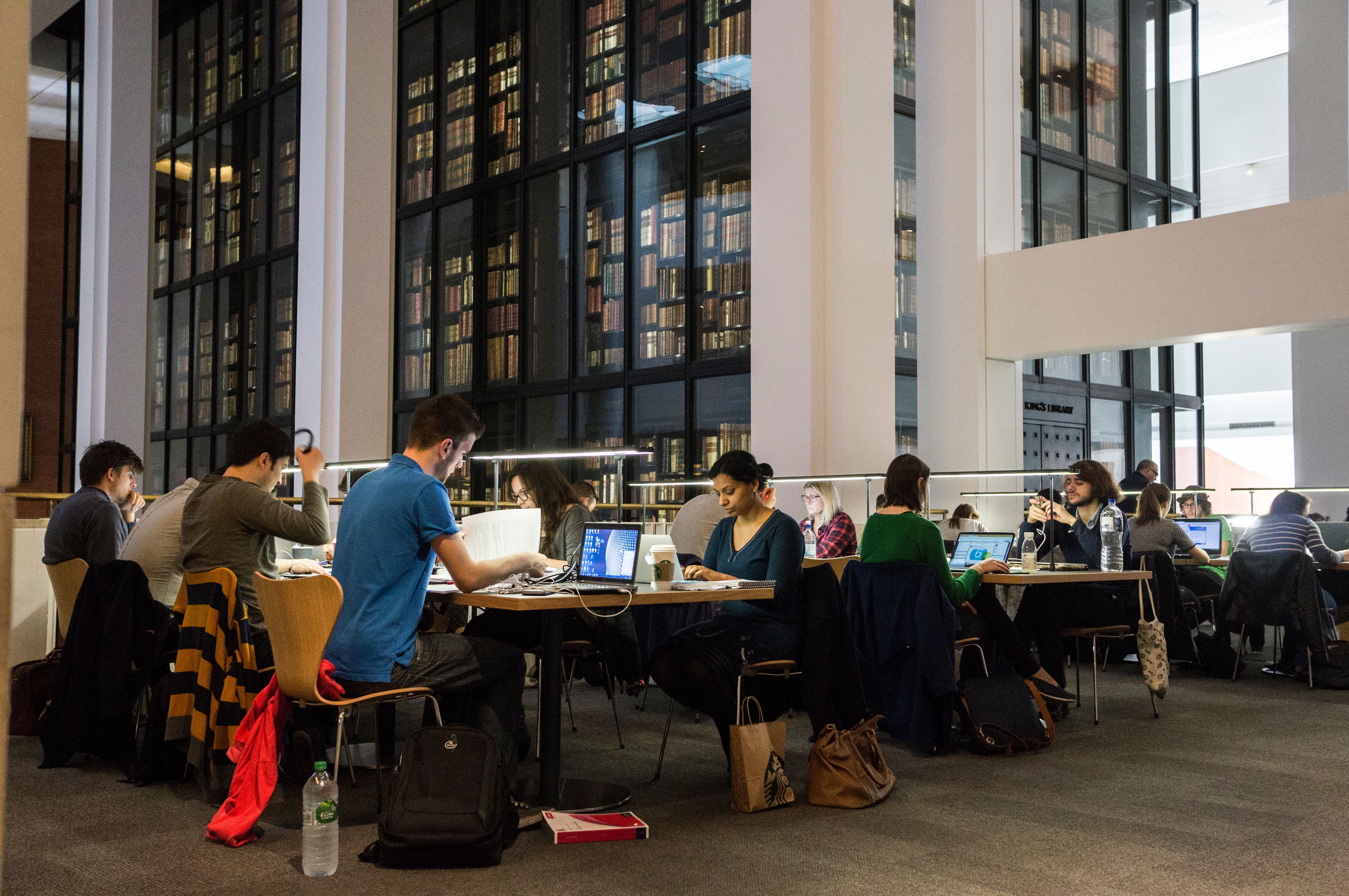 People sit at desks, on their laptops, phones and reading, in the public study space in front of the King's Library at the British Library in London.
