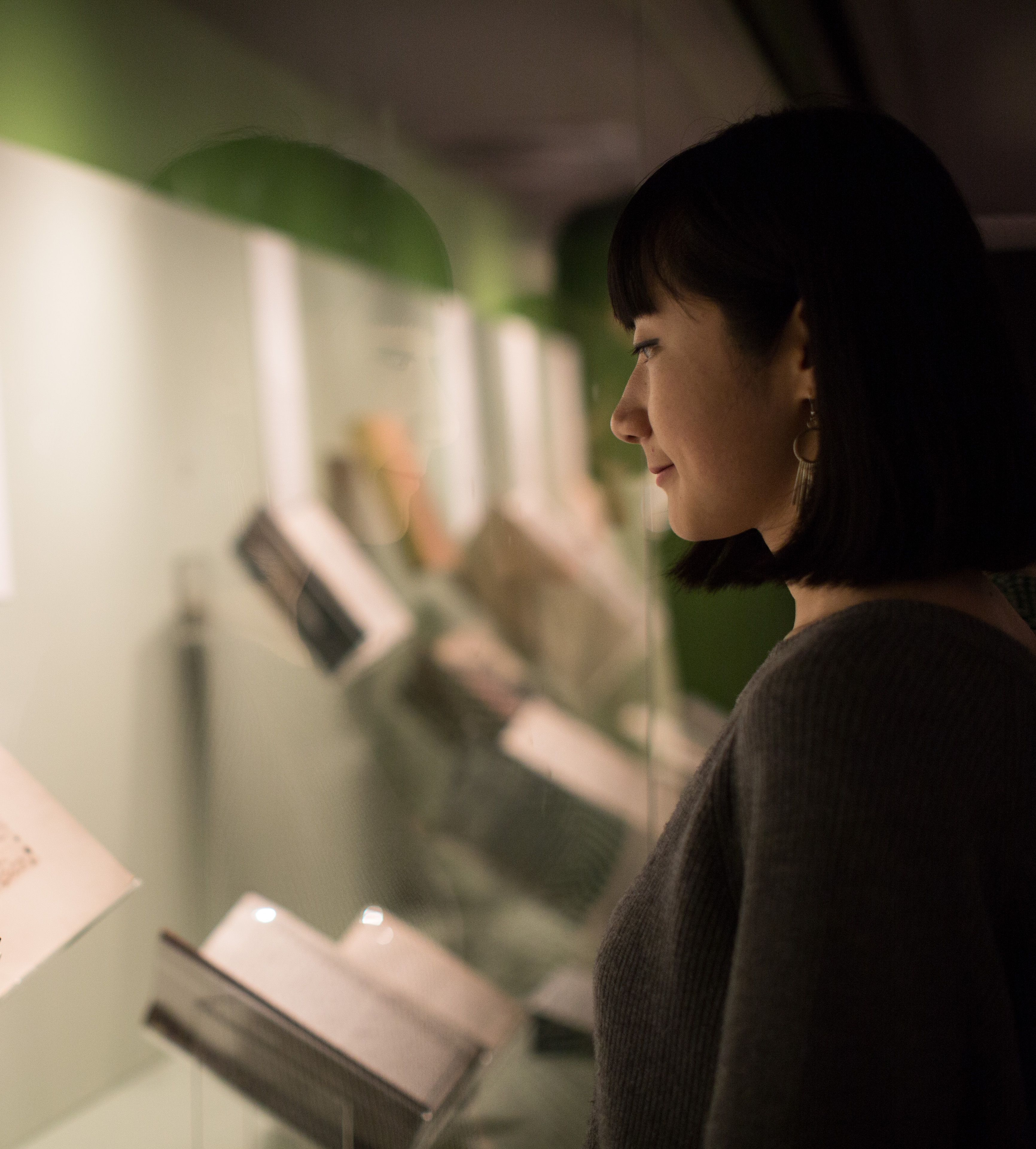 A woman stands looking at an illuminated display case in the Treasures Gallery of the British Library.