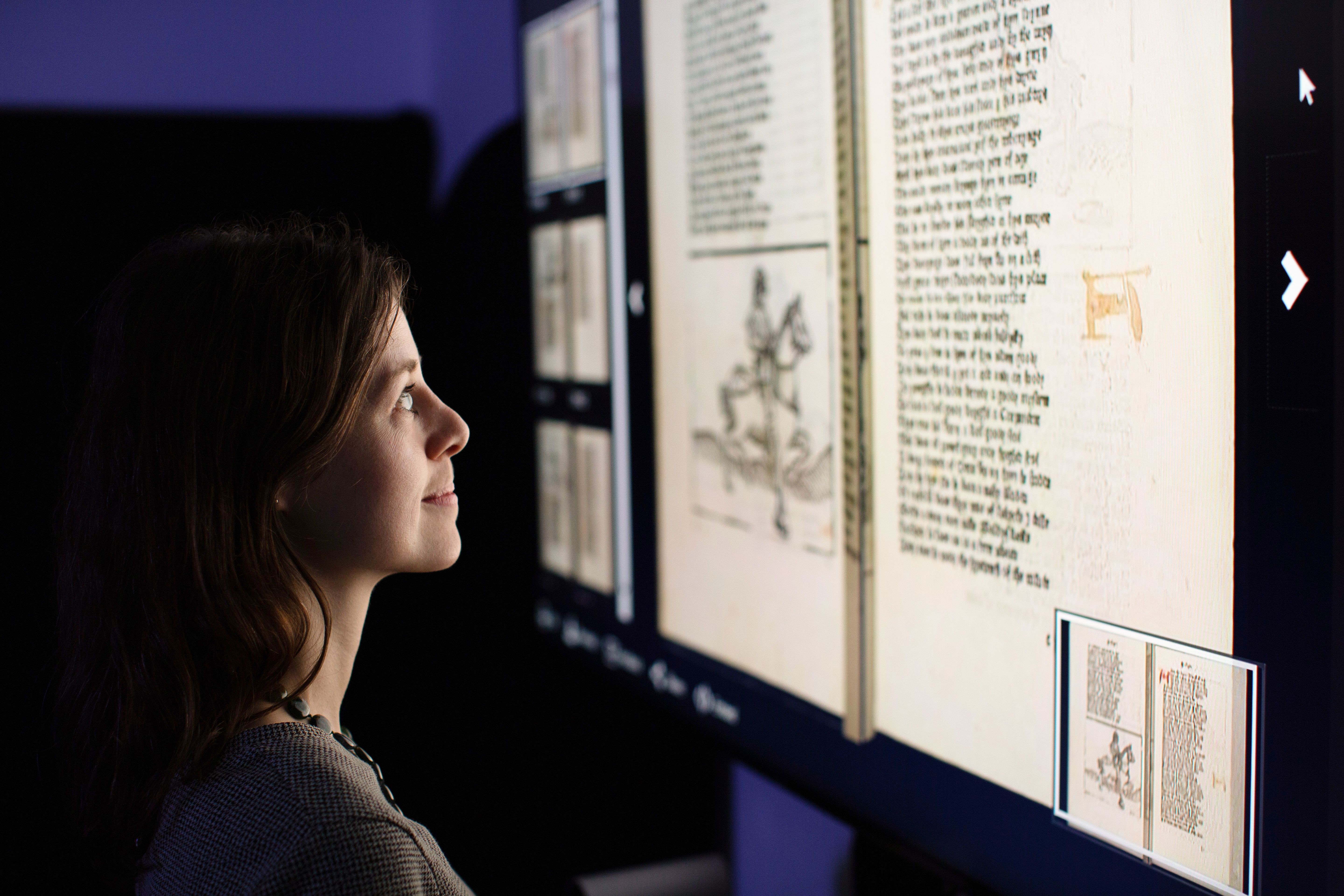 A woman looks at an illuminated display on the wall, showing pages from Chaucer's Canterbury Tales.