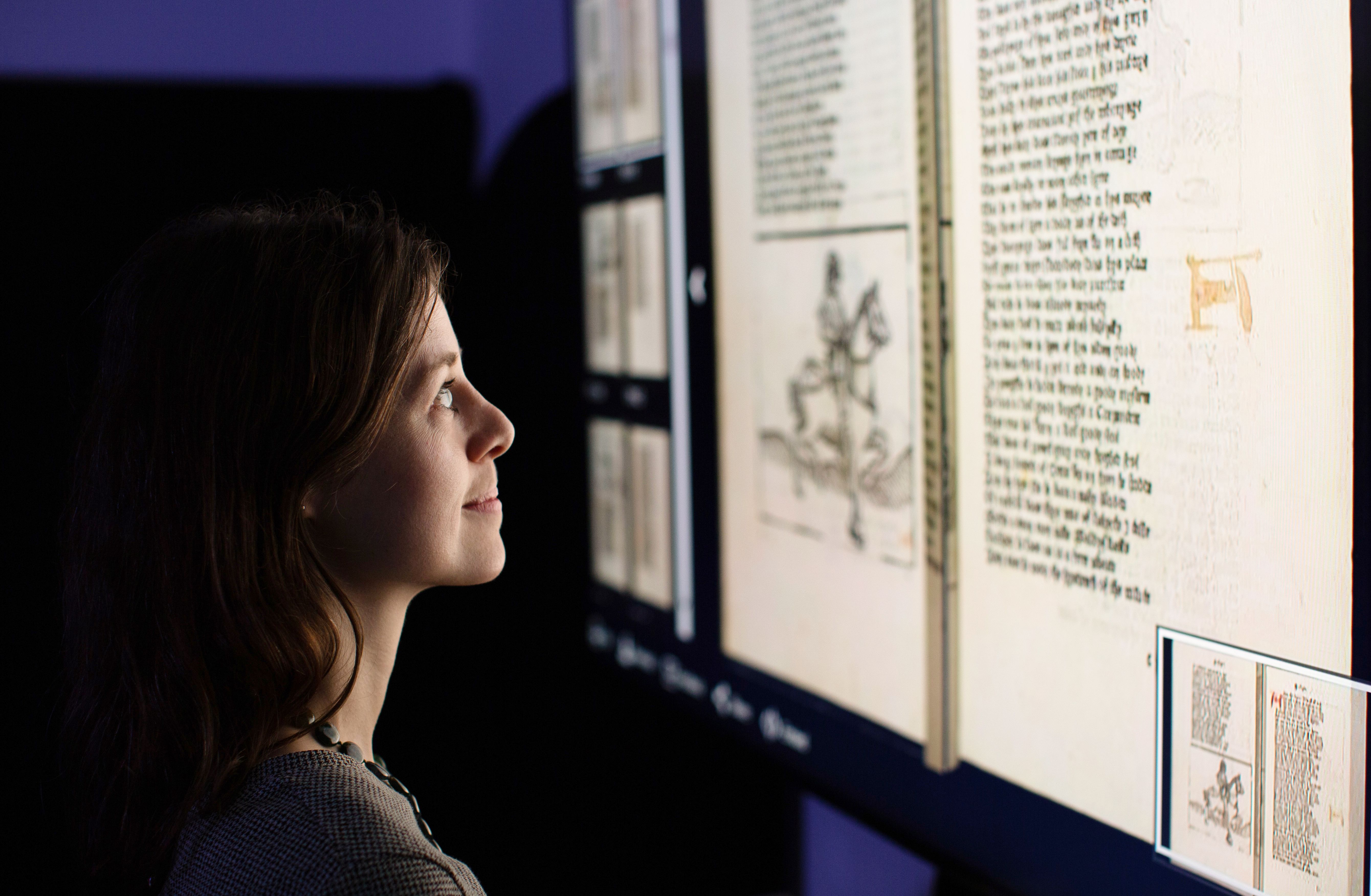 A woman looks at an illuminated display on the wall, showing pages from Chaucer's Canterbury Tales.
