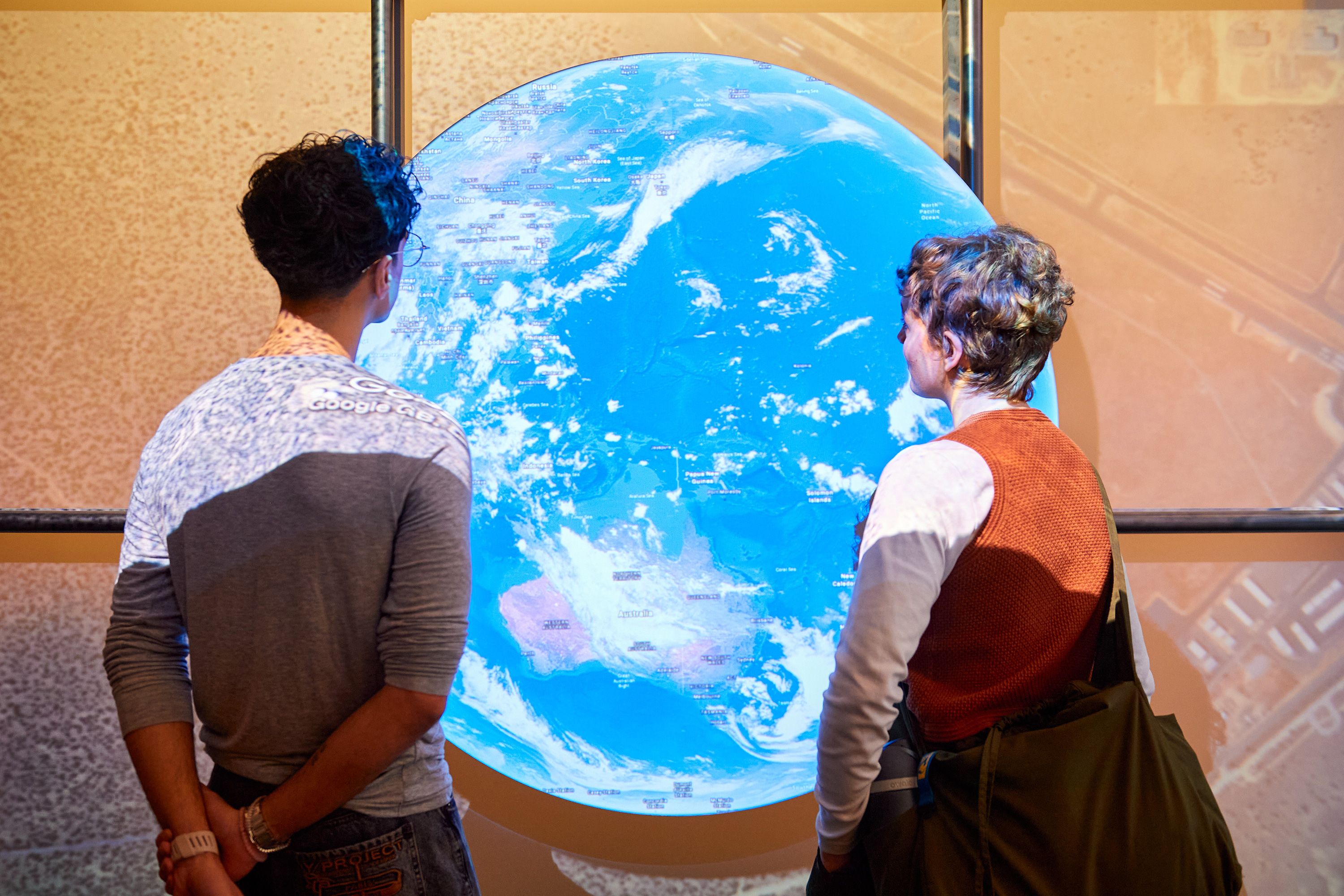 Visitors to the Secret Maps exhibition at the British Library, looking directly at a large installation of Google Earth, over Australia and Asia.