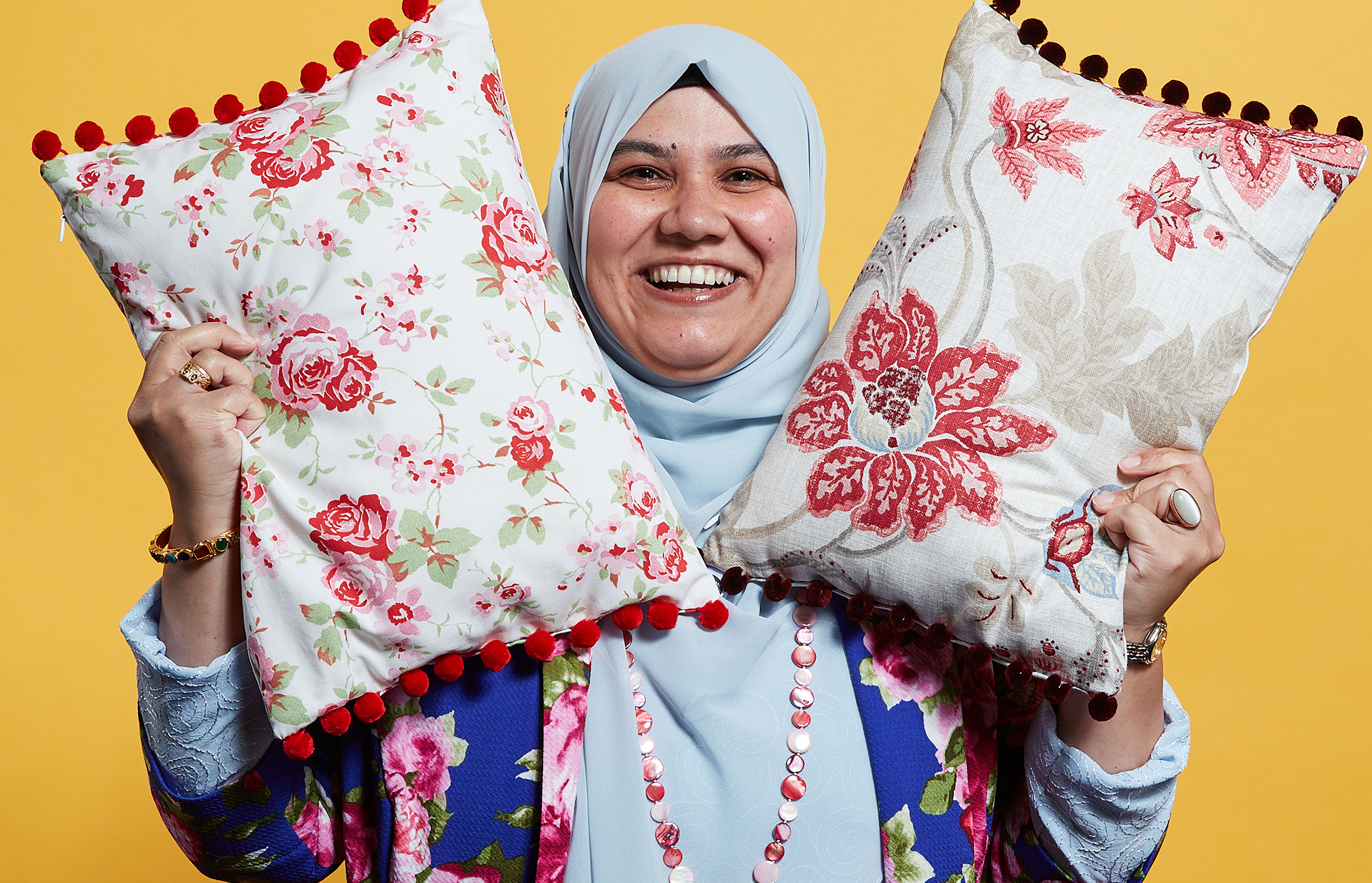 A business woman smiles while holding two cushions in the air to show off her products.