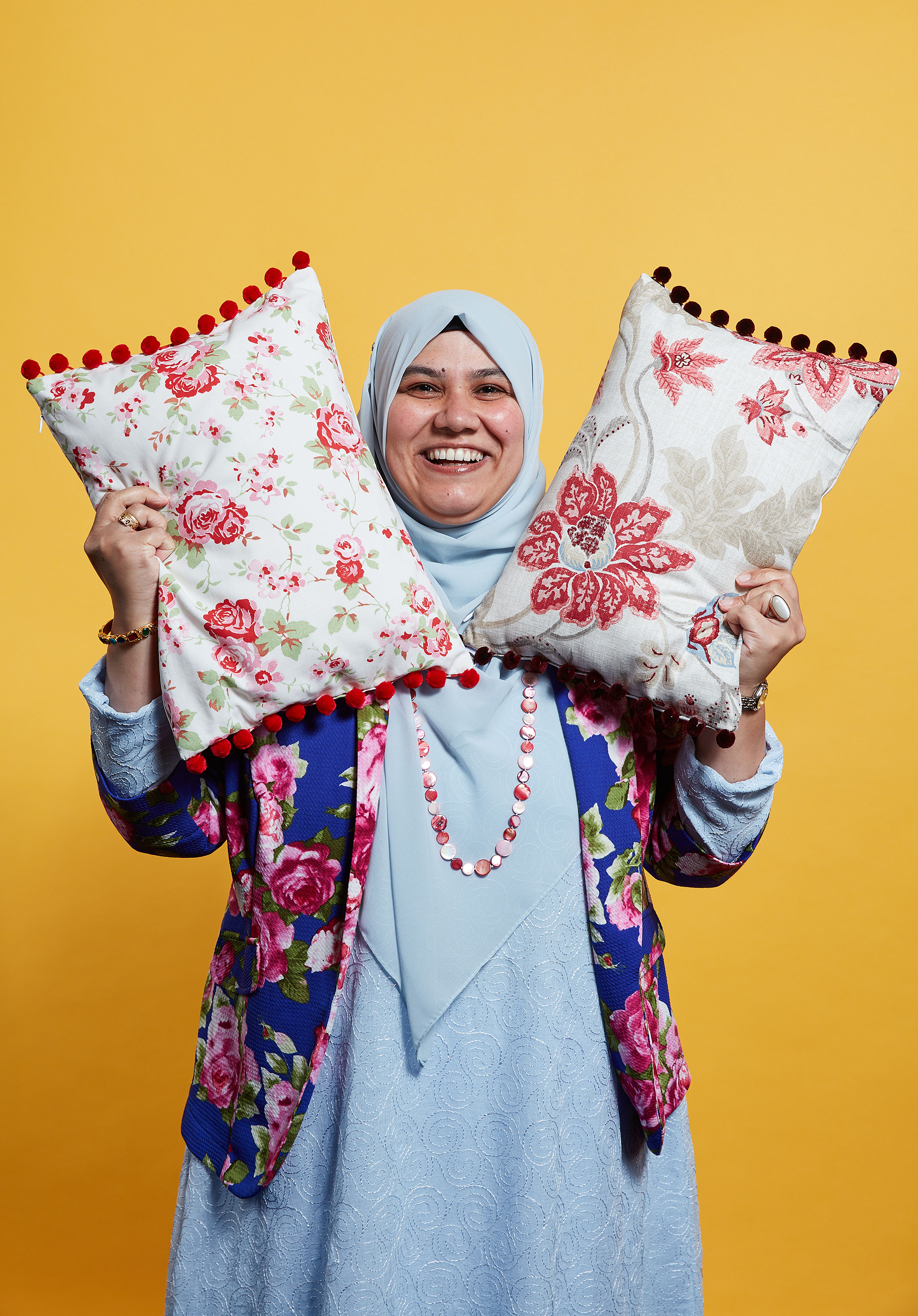 A business woman smiles while holding two cushions in the air to show off her products.