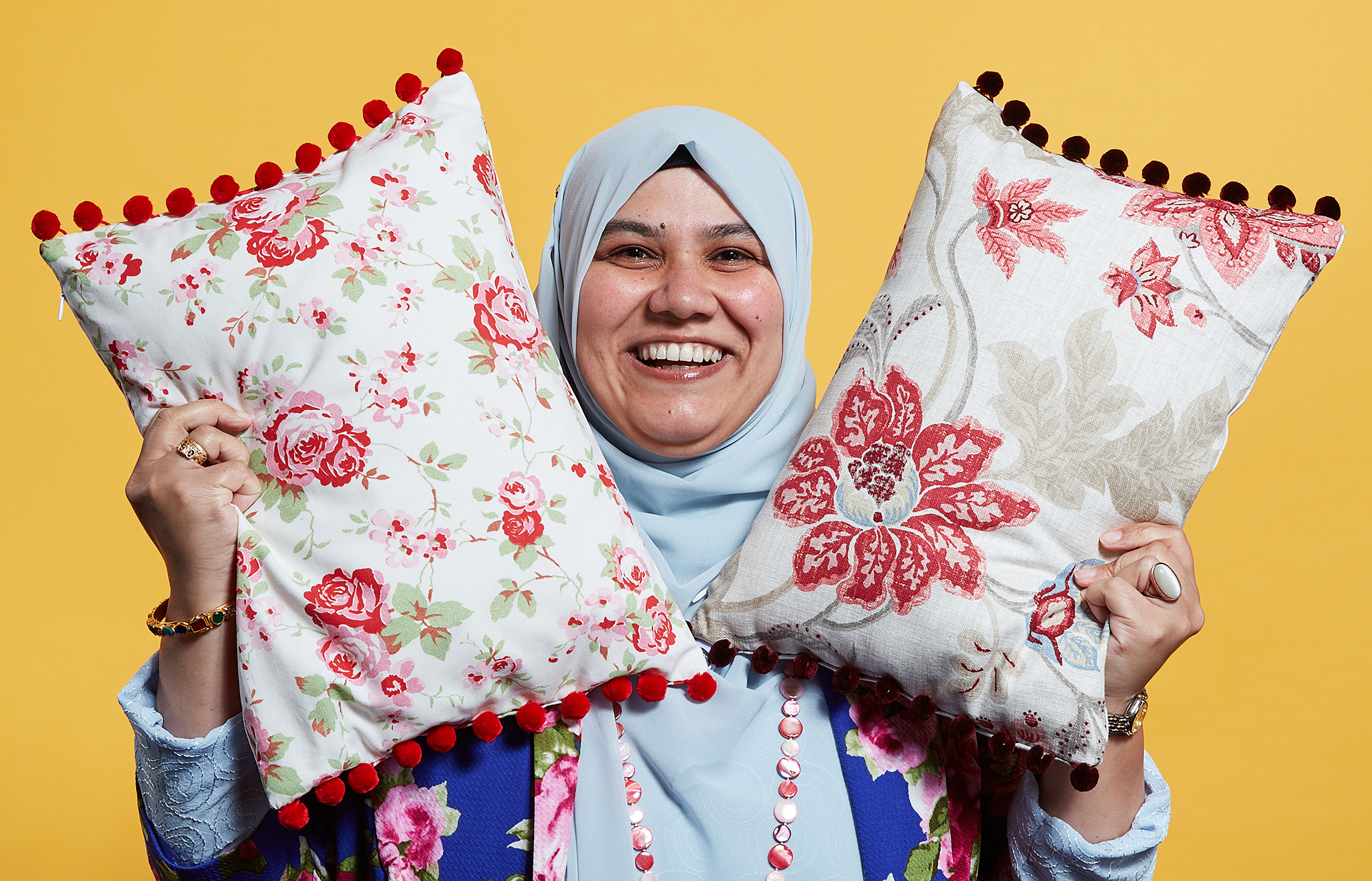 A business woman smiles while holding two cushions in the air to show off her products.