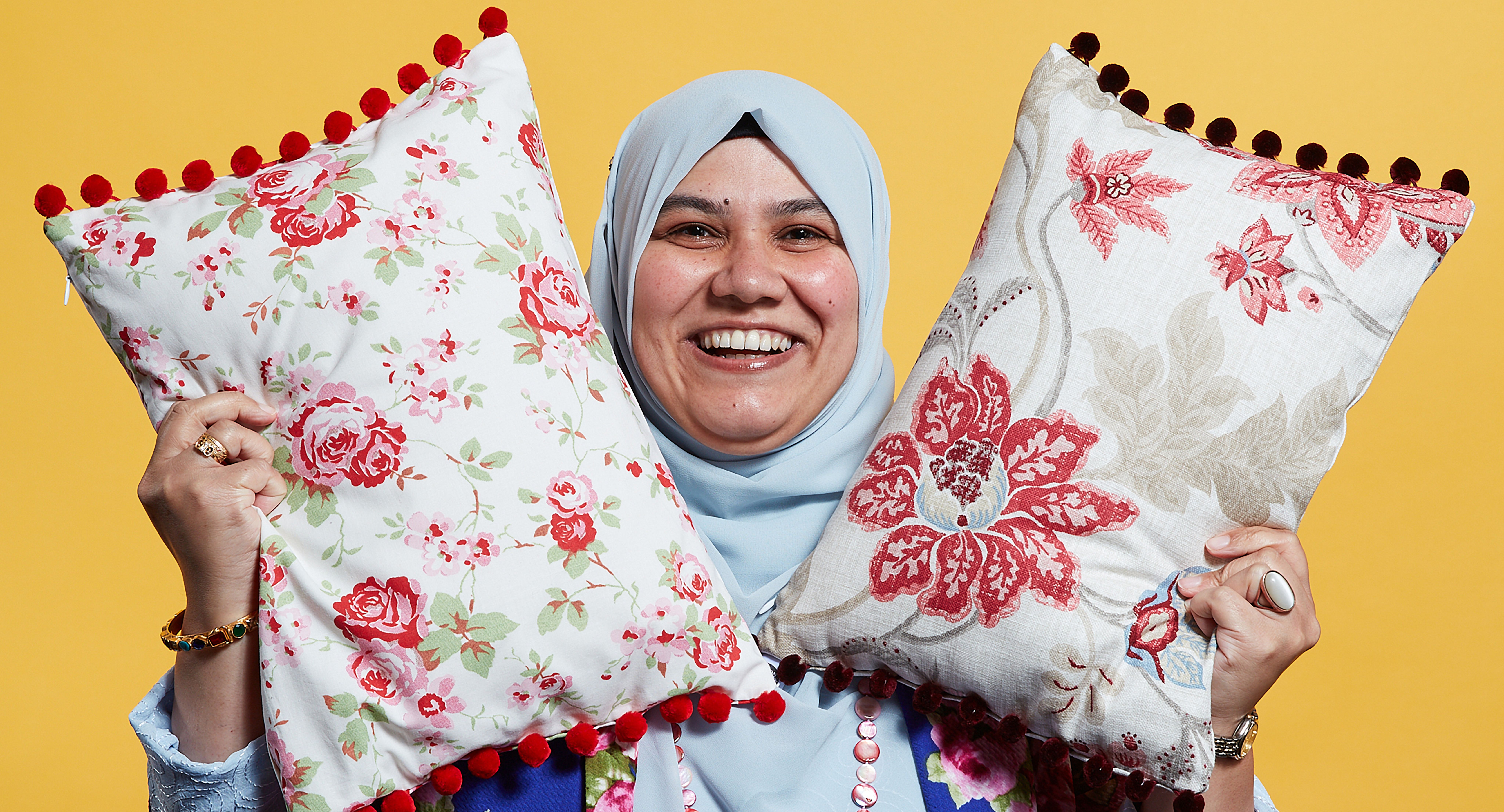 A business woman smiles while holding two cushions in the air to show off her products.