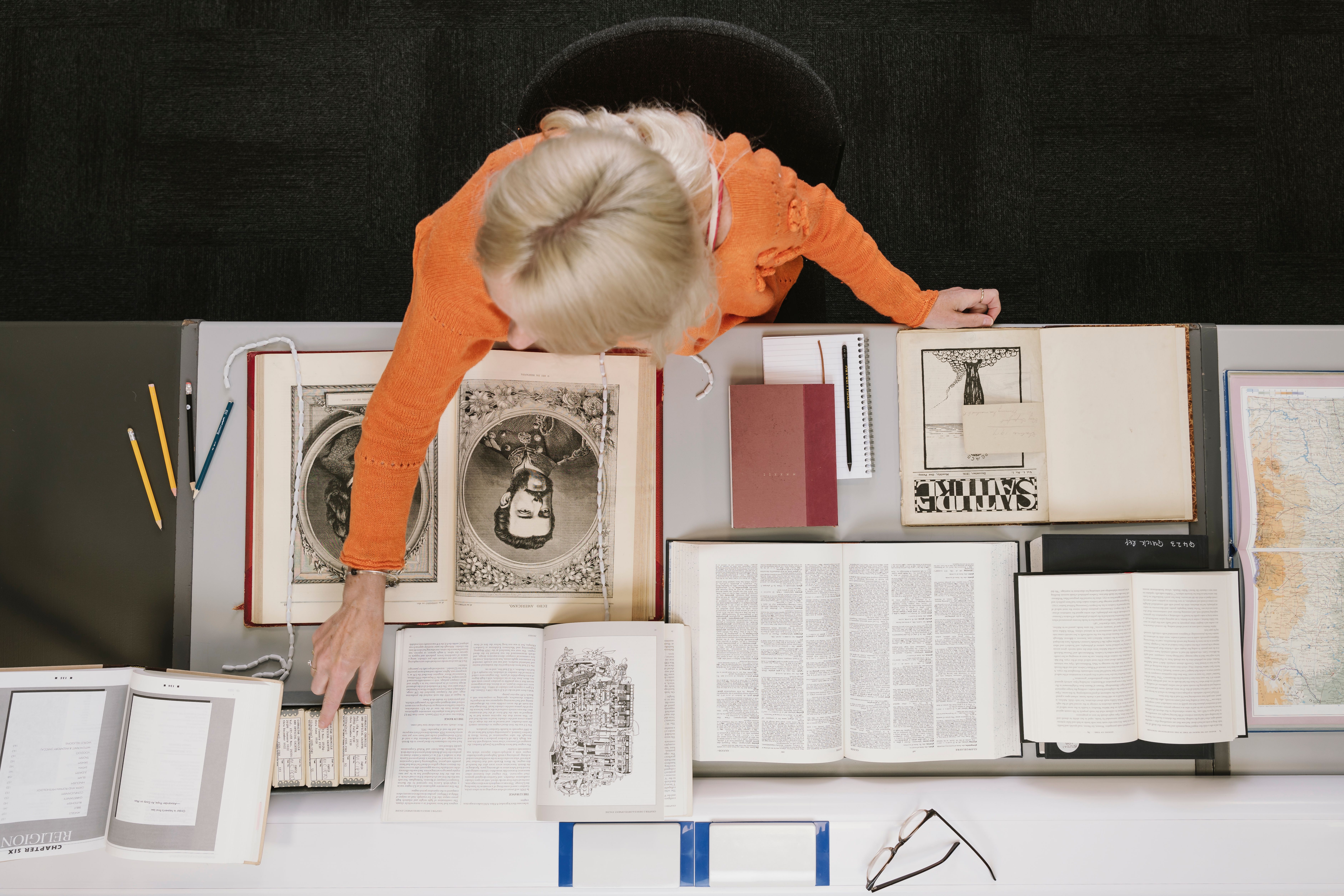 A view of a woman from above. She sits at a desk in the British Library Boston Spa Reading Room, consulting a number of open books.