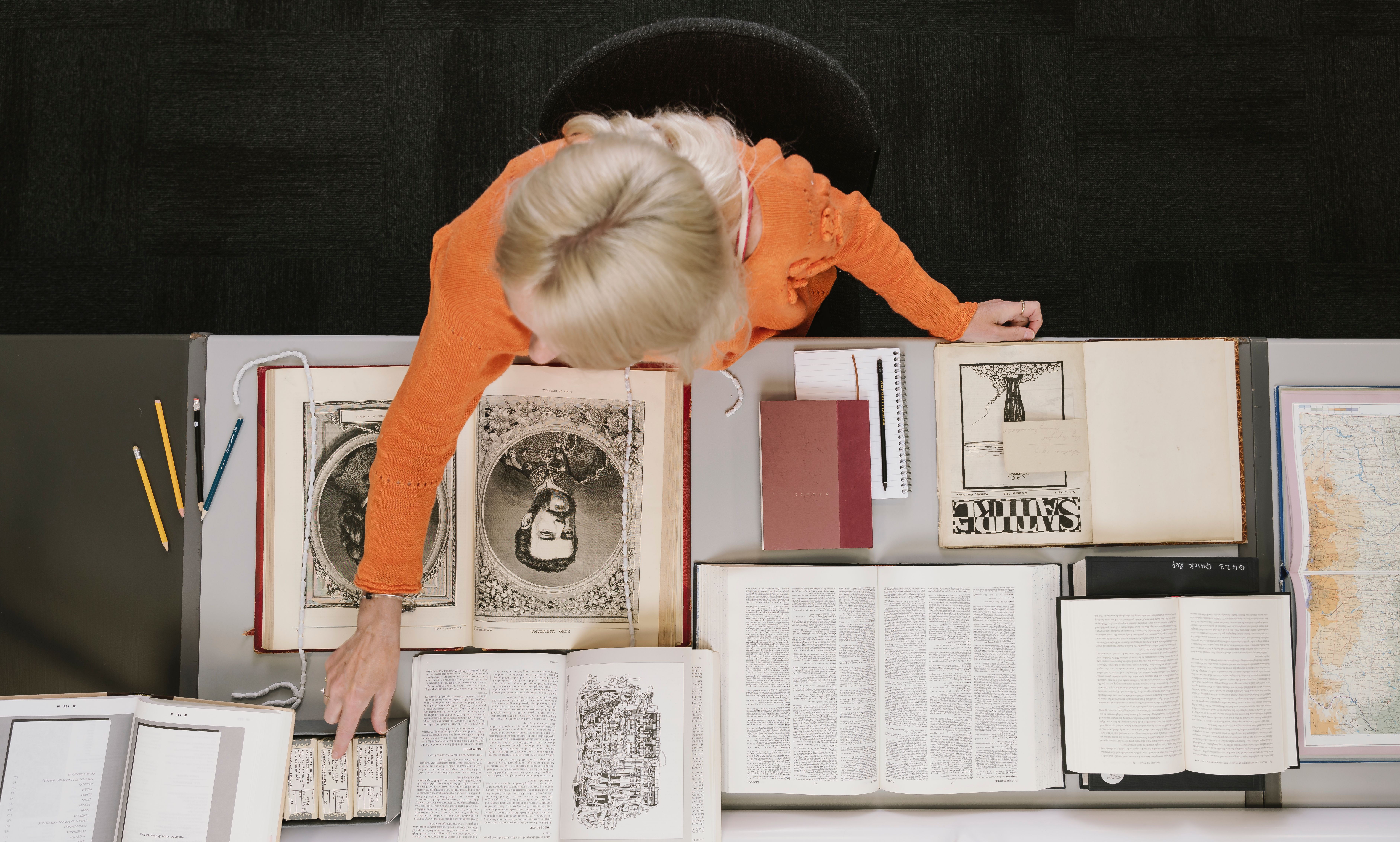 A view of a woman from above. She sits at a desk in the British Library Boston Spa Reading Room, consulting a number of open books.