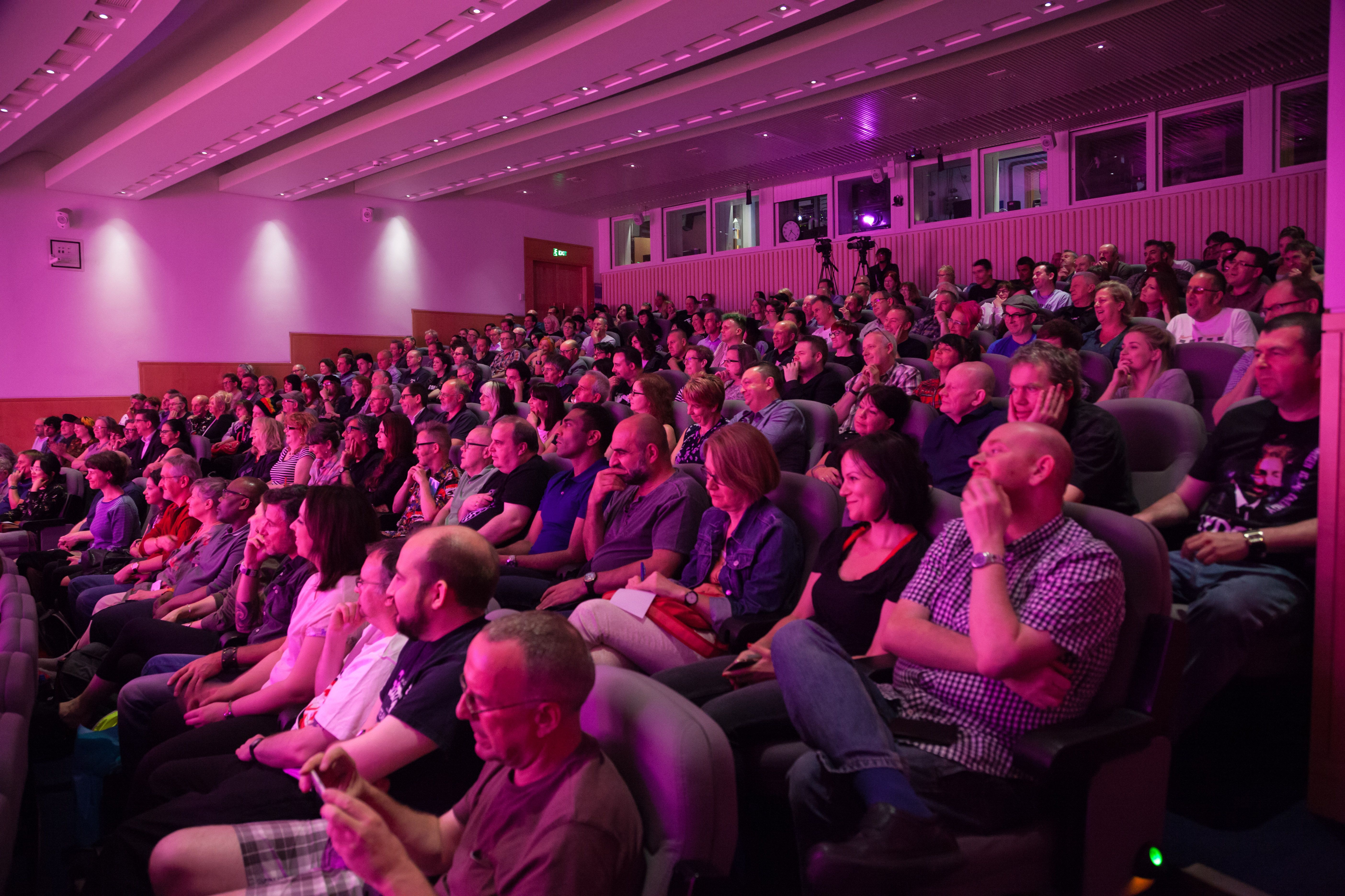 An audience of people sit under pink lights in the Knowledge Centre auditorium in the British Library in London