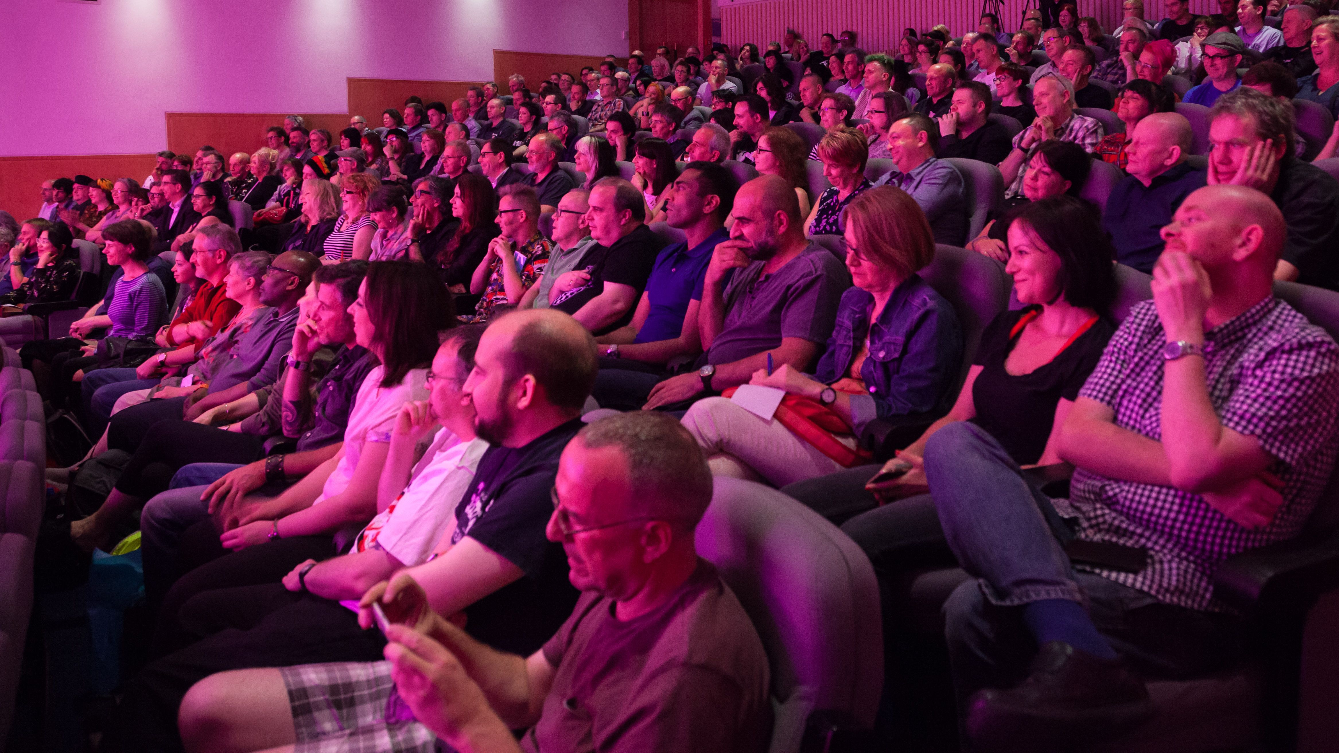 An audience of people sit under pink lights in the Knowledge Centre auditorium in the British Library in London