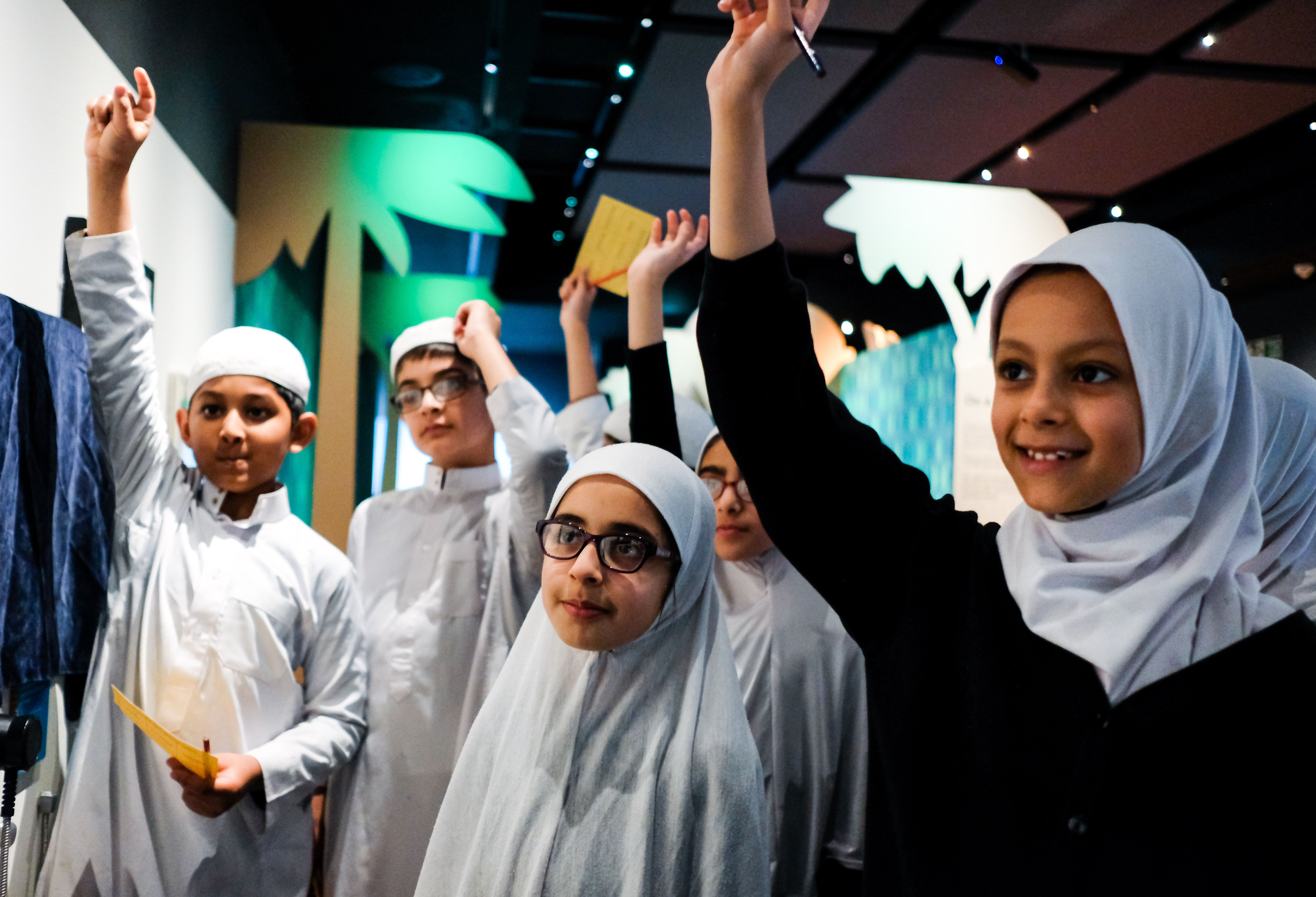 A group of school children stand with their hands raised at a school event at the British Library.