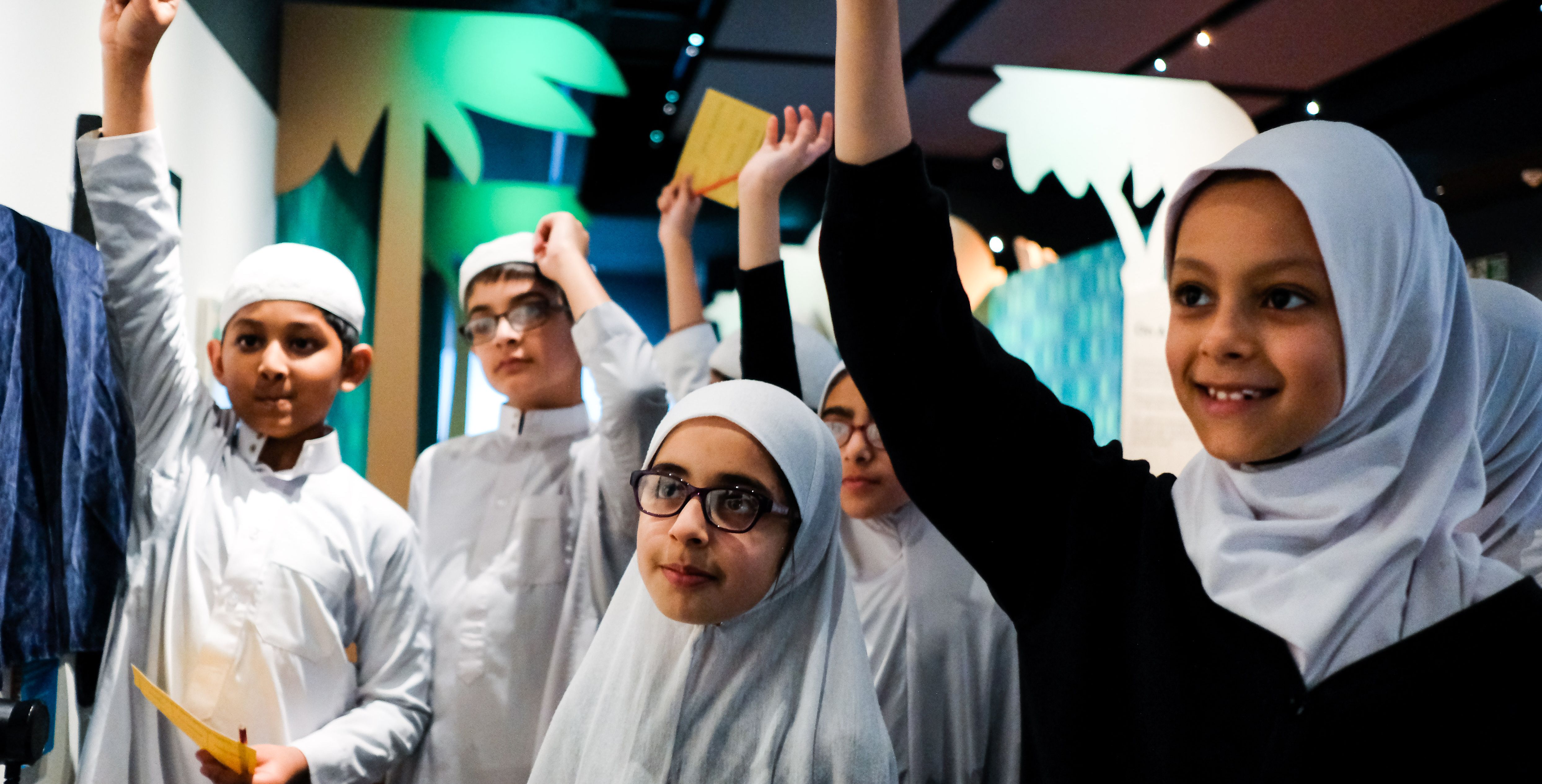 A group of school children stand with their hands raised at a school event at the British Library.