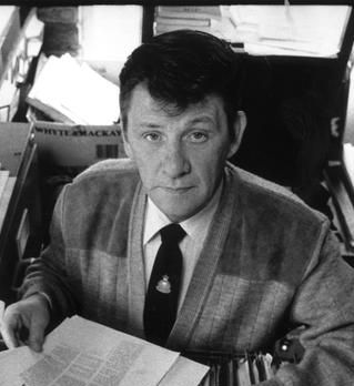 Ken McGinley looks up at the camera with a document in his hand whilst sat at a desk.