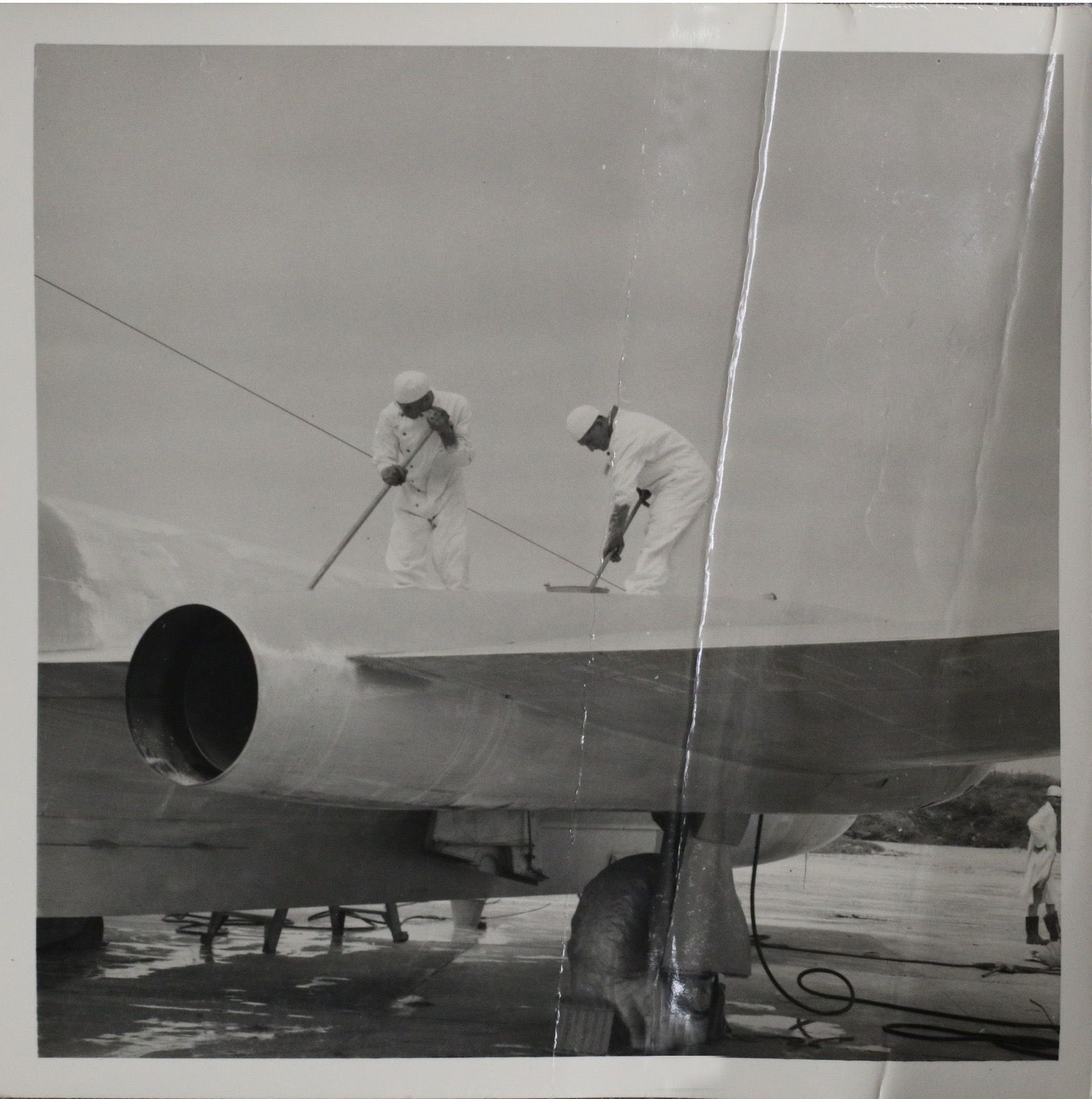 Two men wearing protective equipment stand on and scrub the wing of a Canberra.