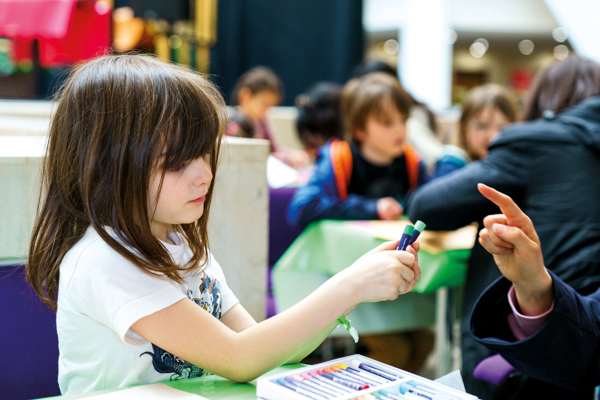 A young girl uses crayons for an activity, alongside other children, at the British Library in London.