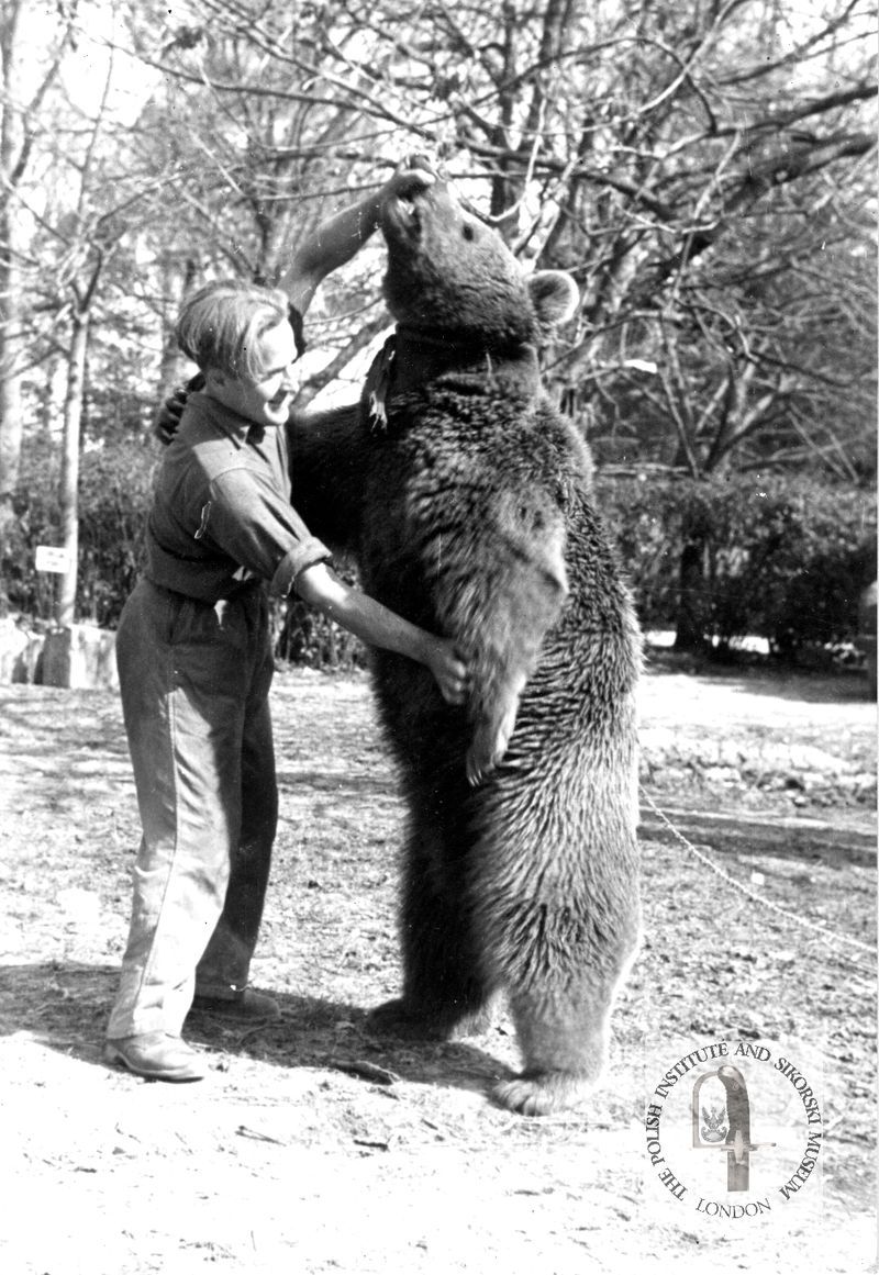 A soldier dancing with a bear who is standing on up on its hind legs.