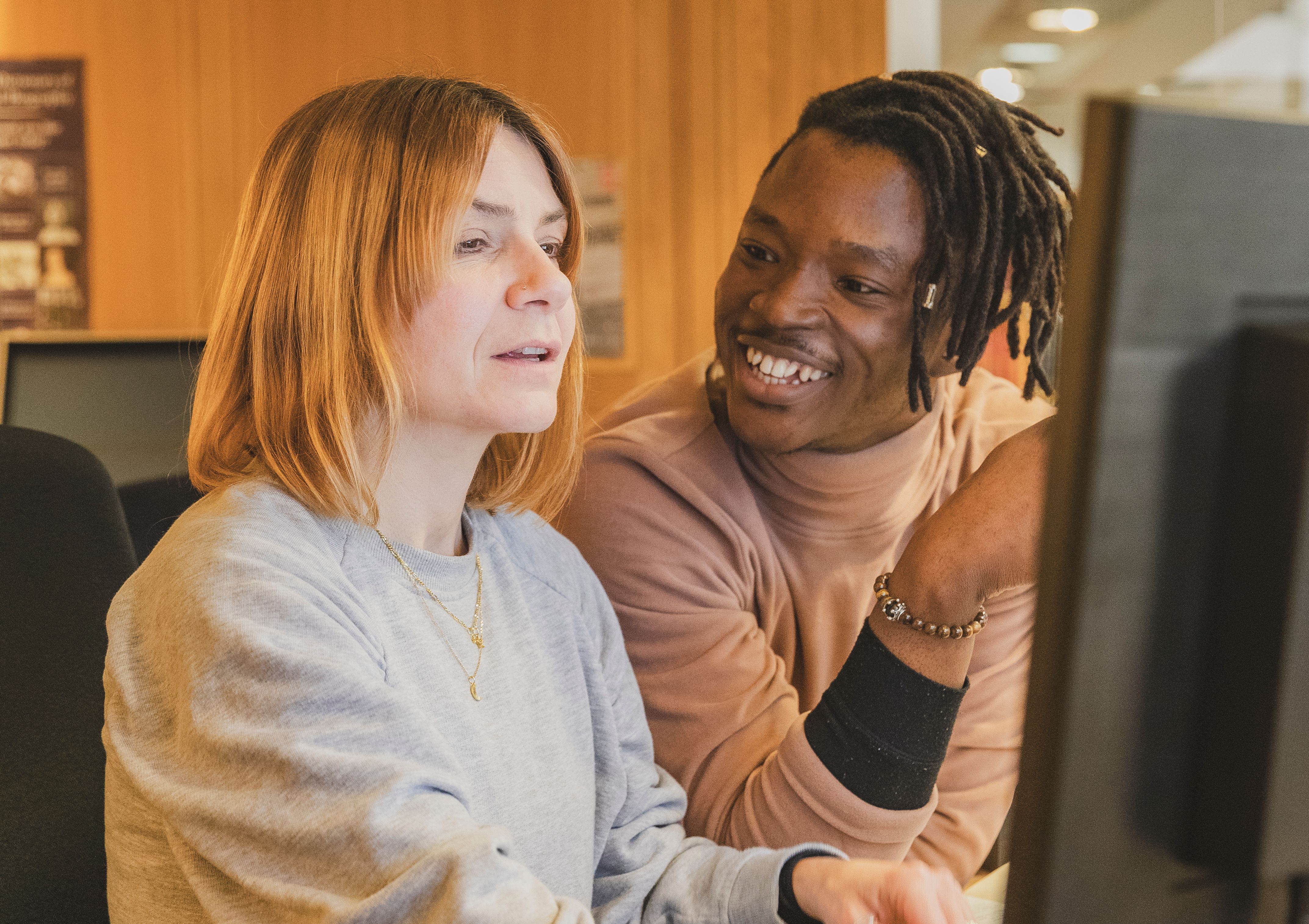 A young man talks to a woman in front of a computer screen at the Reading Room helpdesk in the British Library in London