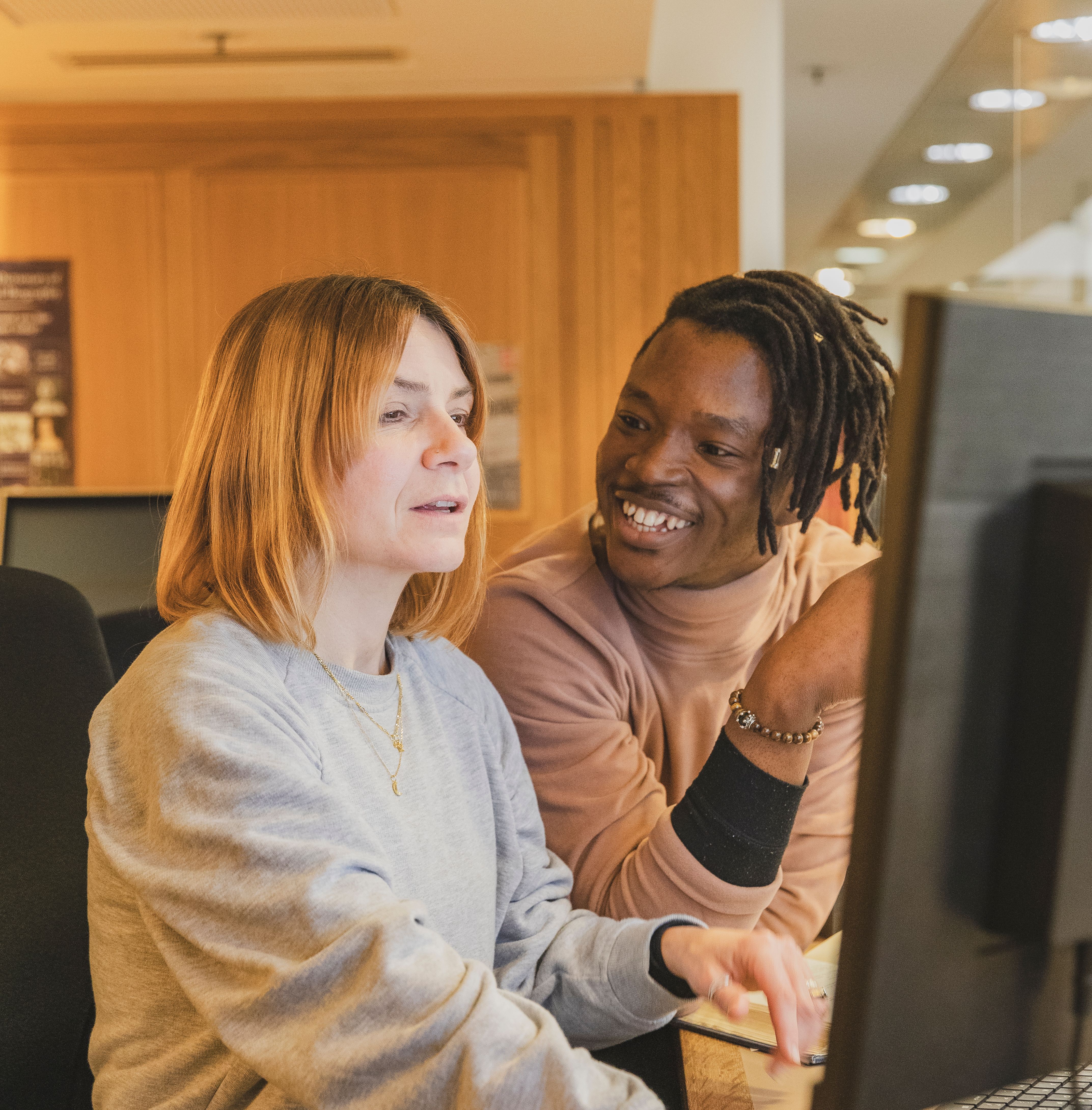 A young man talks to a woman in front of a computer screen at the Reading Room helpdesk in the British Library in London