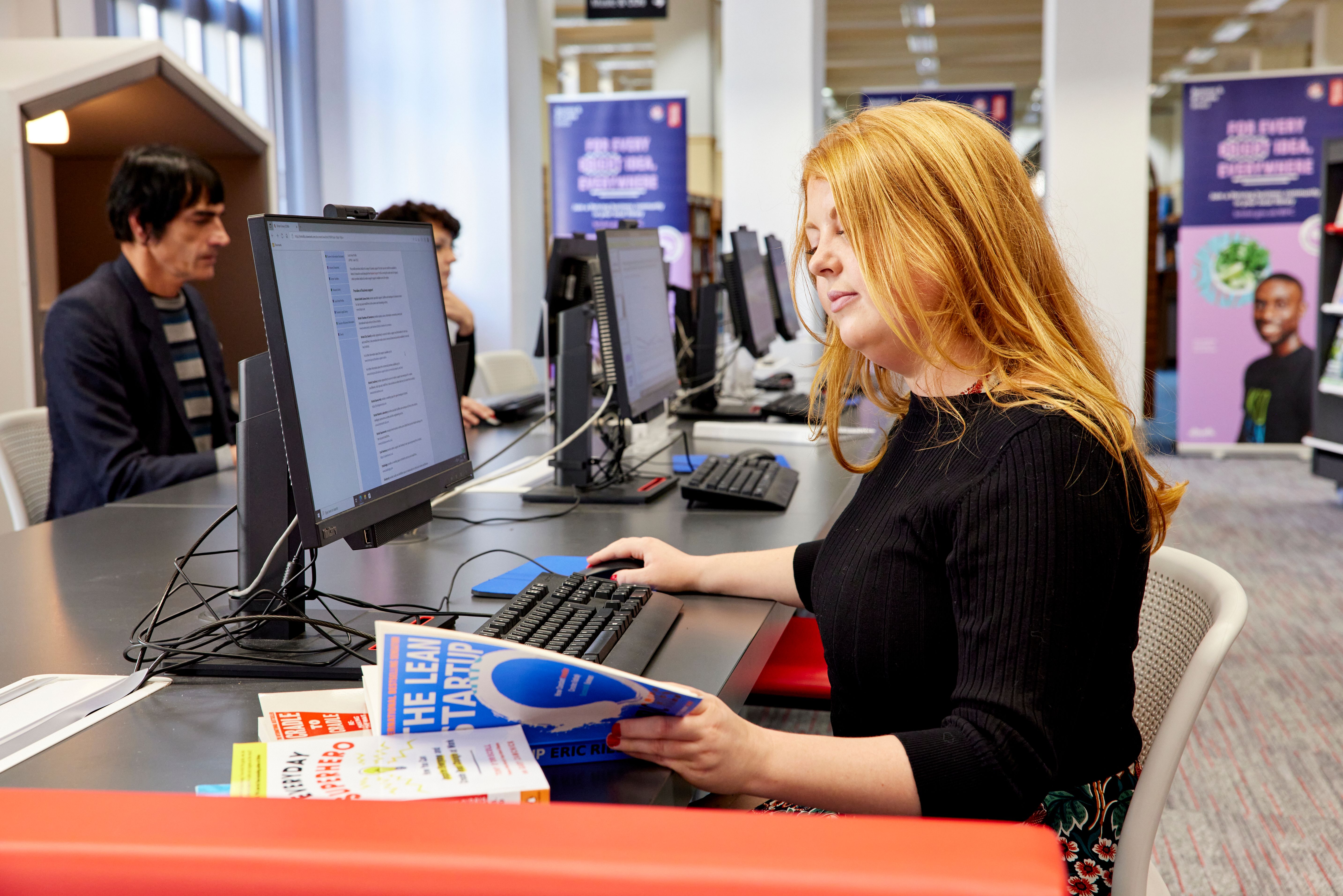 A business woman sits and consults resources at a Business & IP Centre in Bristol.