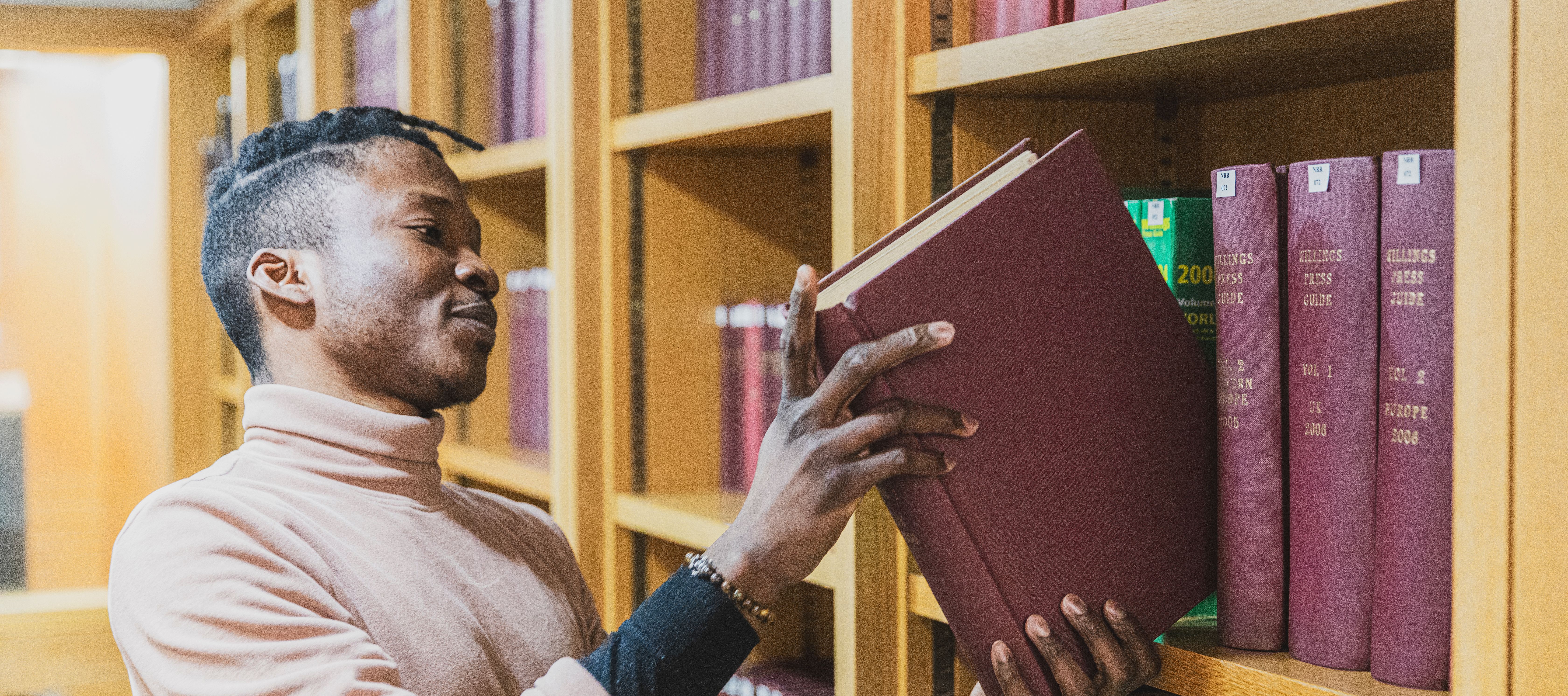 An apprentice carefully places a book on a book shelf at the British Library