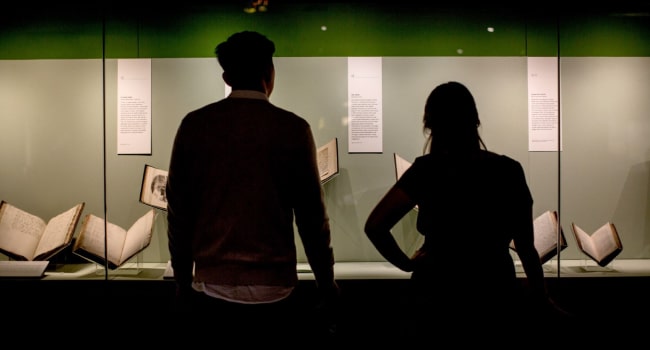 Two people stand looking at a display cabinet at a British Library exhibition
