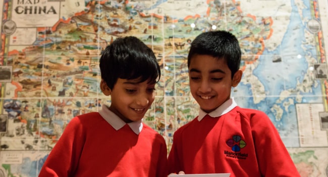 Two children stand in front of a map